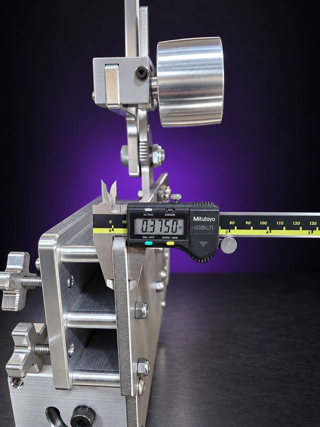 Calipers reading 0.375 inch across the chassis plate, with the tensioner and idler wheel behind, on black with a purple glow