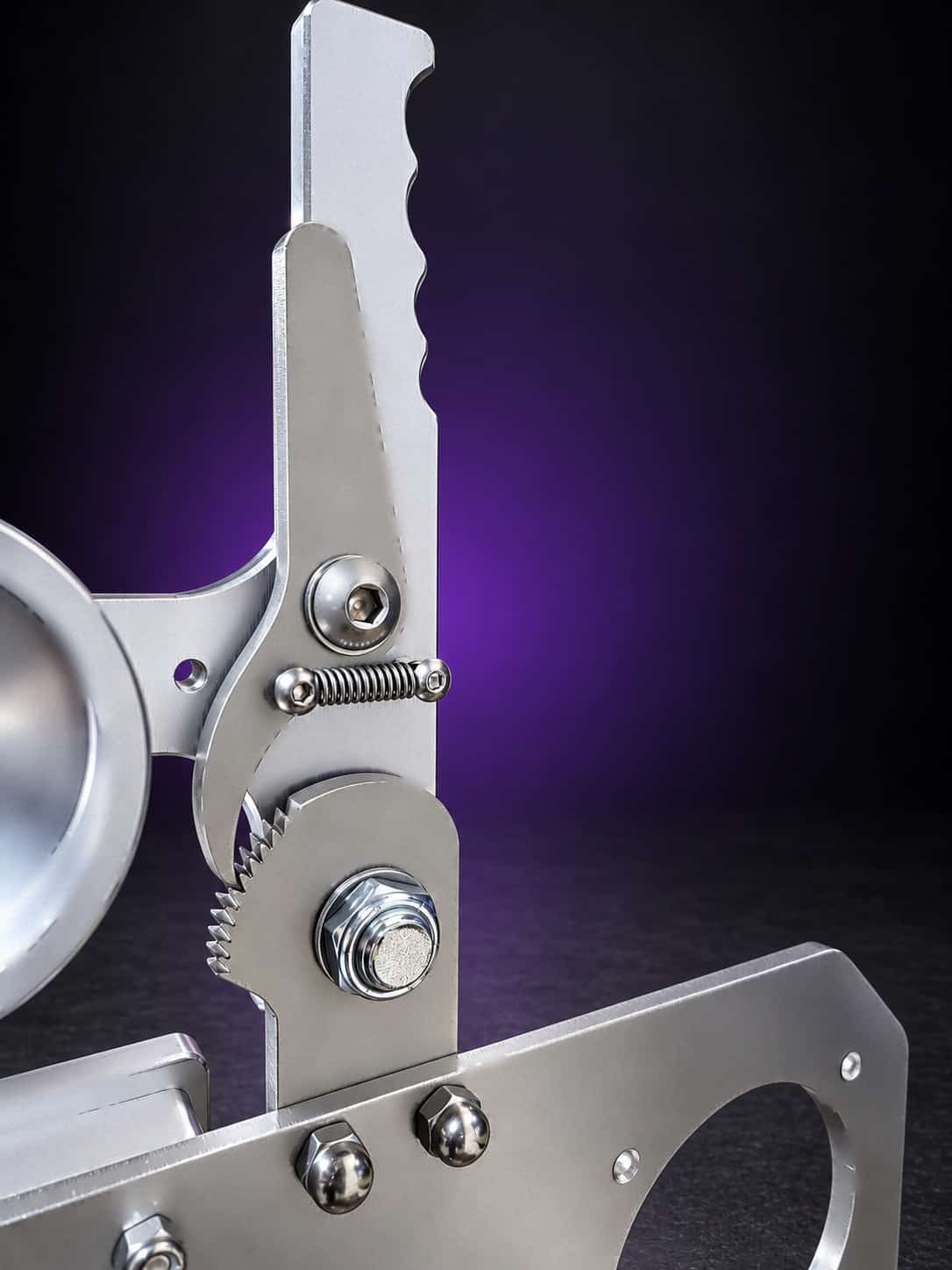 Ratchet belt tensioner on the steel Torus grinder: spring pawl and toothed cam, close-up, on black with a purple glow