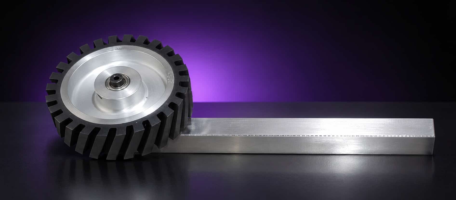 Serrated rubber contact wheel with aluminum hub and bearing on a square tooling arm, side view, on black with a purple glow
