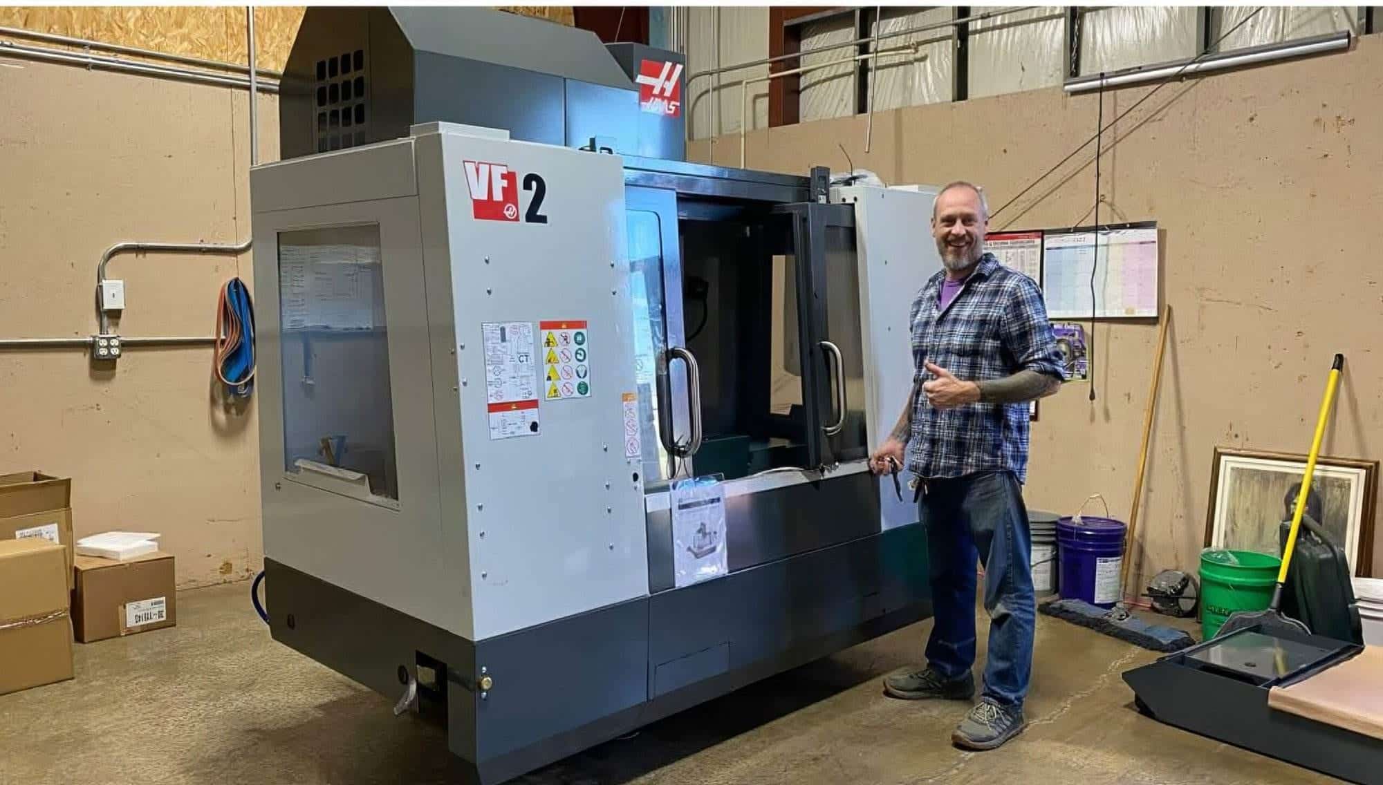 Rich from Torus CNC giving a thumbs up next to the shop's Haas VF-2 CNC mill