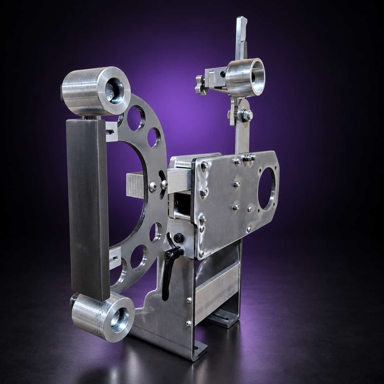 Torus steel 2x72 grinder, close view from the platen side: platen bar, drilled arm, motor plate, on black with a purple glow