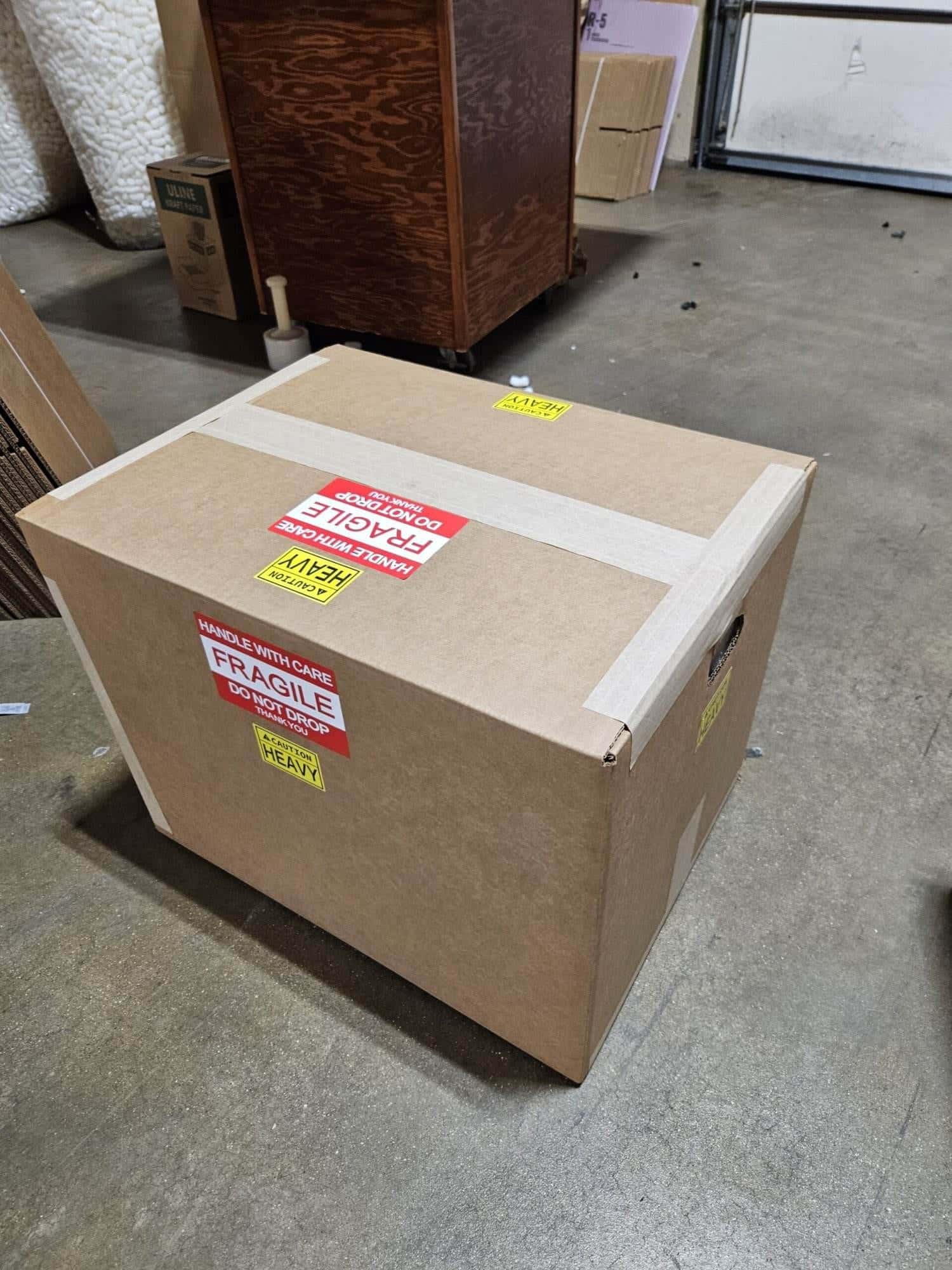 A taped shipping box labelled FRAGILE and HEAVY on the shop floor, ready to go out