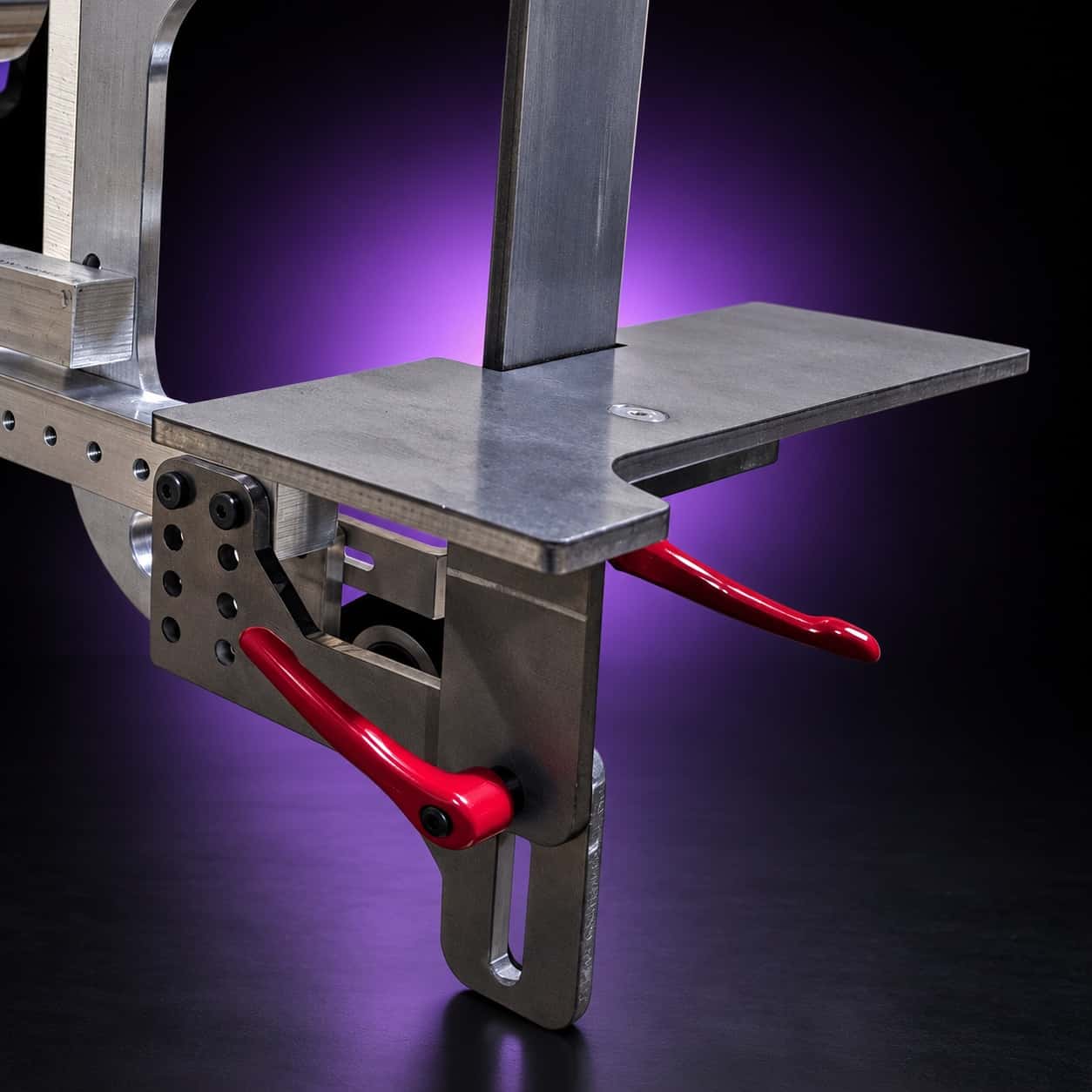Adjustable work table on the tool arm, with its slotted bracket and two red cam levers, on black with a purple glow