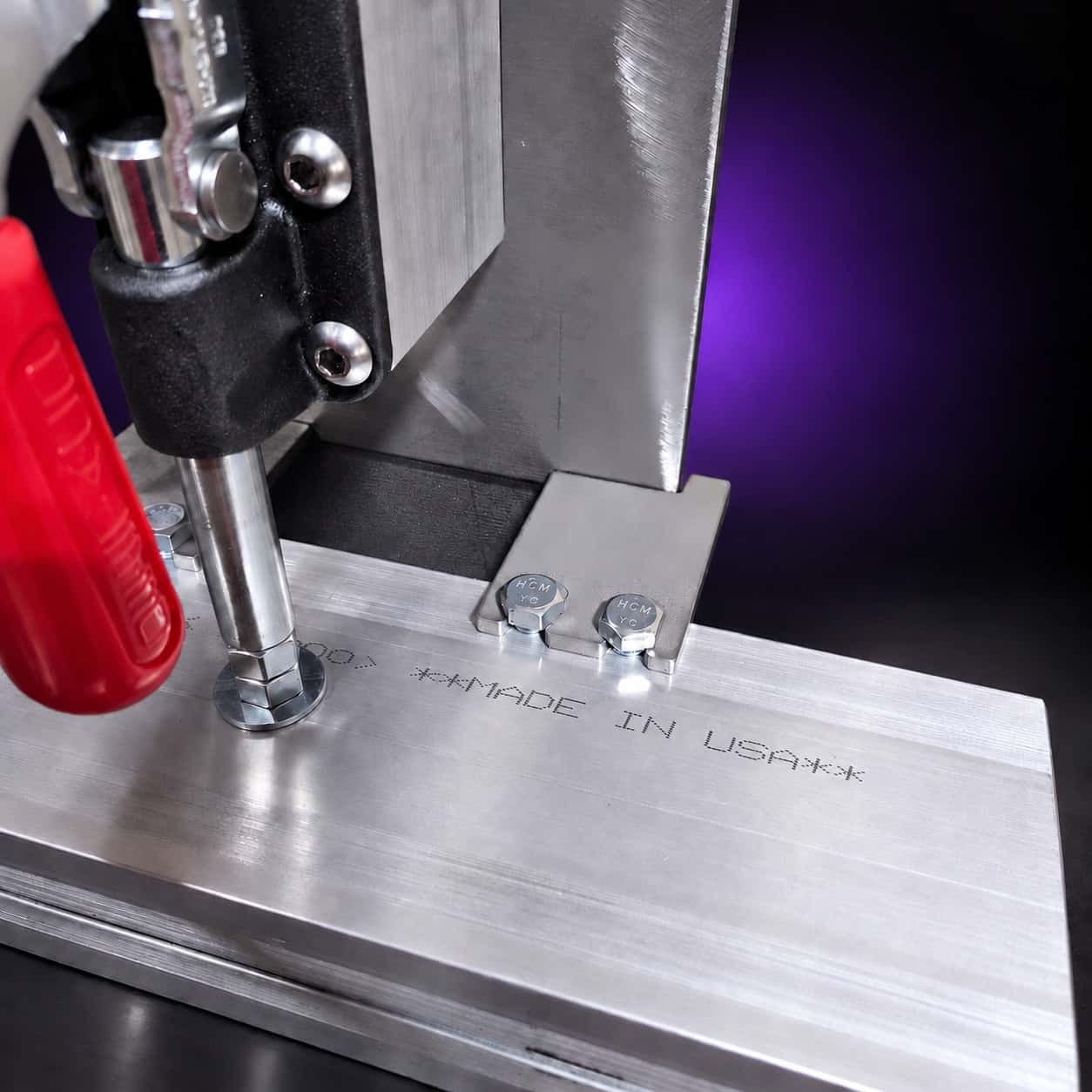 Quench vise toggle clamp, mounting tabs and Made in USA marking on the top plate, close-up, on black with a purple glow