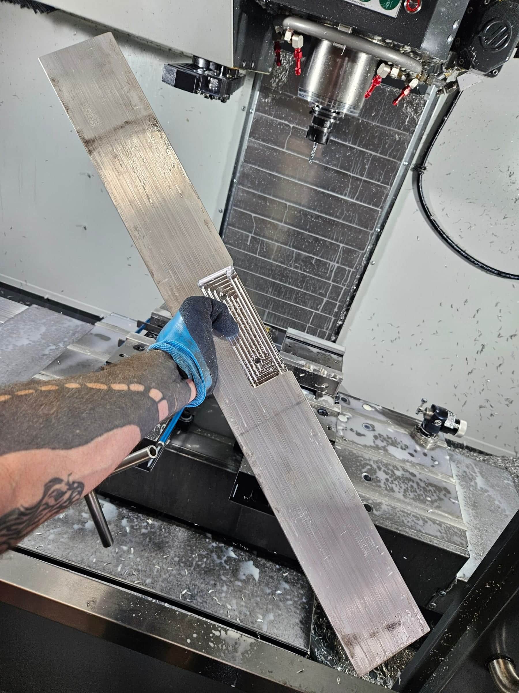 A hand holding a freshly machined aluminum quench plate inside the coolant-misted mill