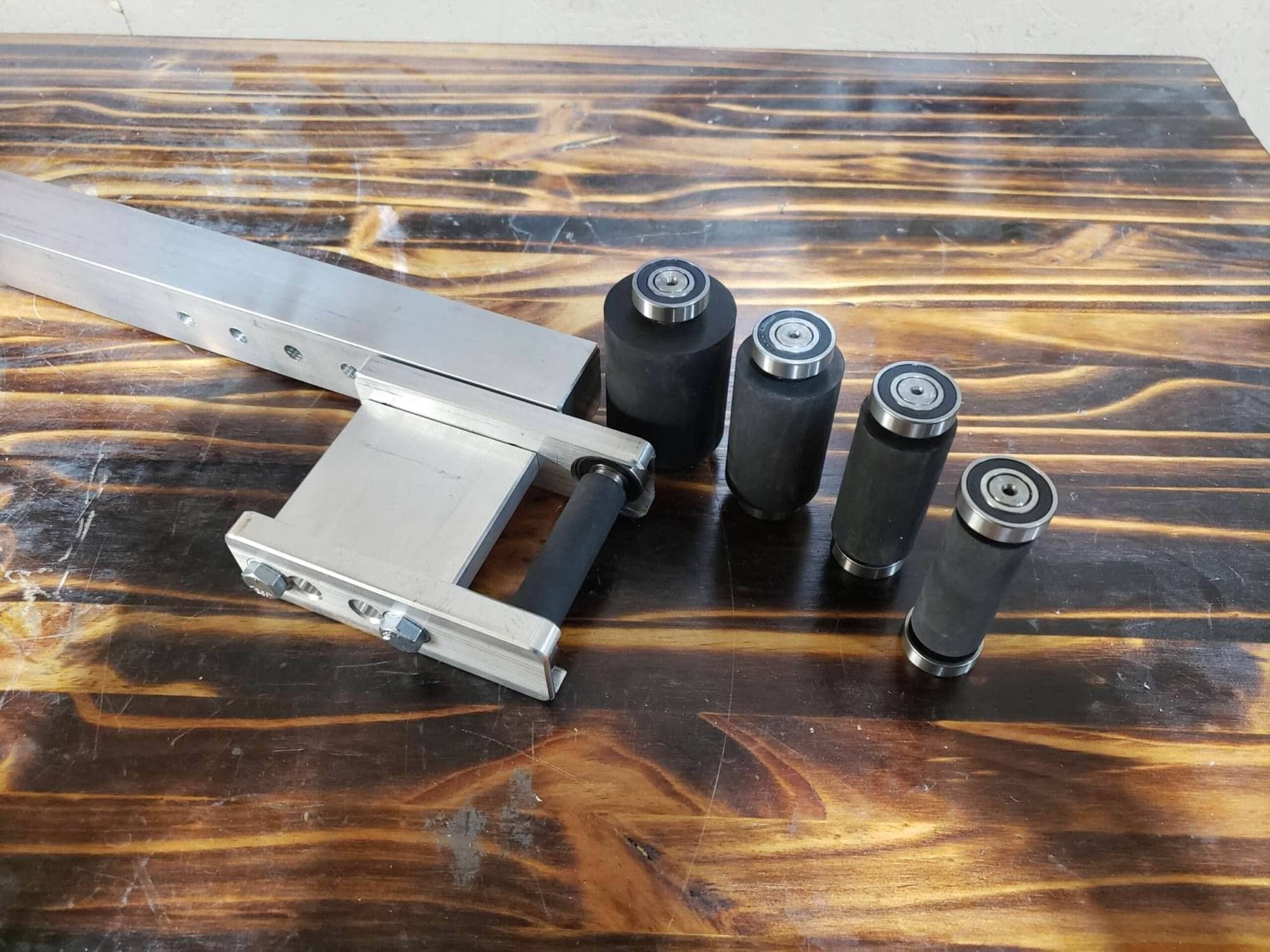 The small wheel attachment on its aluminum tooling arm beside four rubber wheels in graduated sizes, on a wood bench