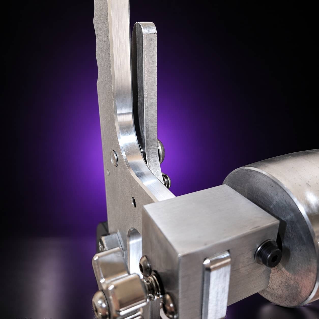 Tension lever, clamp block and aluminum idler wheel on the Torus steel 2x72 grinder, close-up, on black with a purple glow