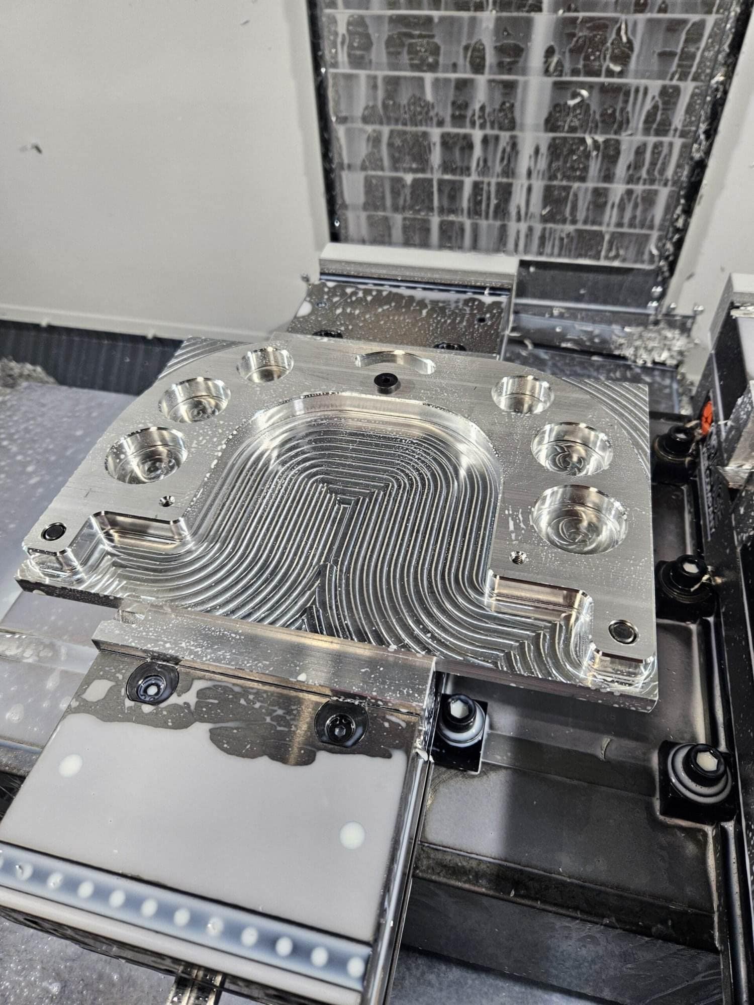 Freshly CNC-machined aluminum mounting plate with coolant droplets sitting on the mill table