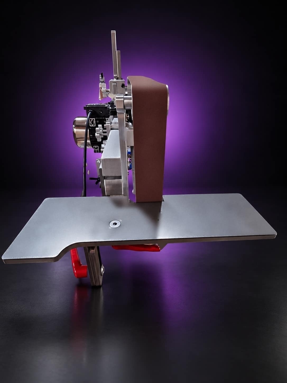 Work table in front of the belt, side-on view, with red cam levers under the plate, on black with a purple glow