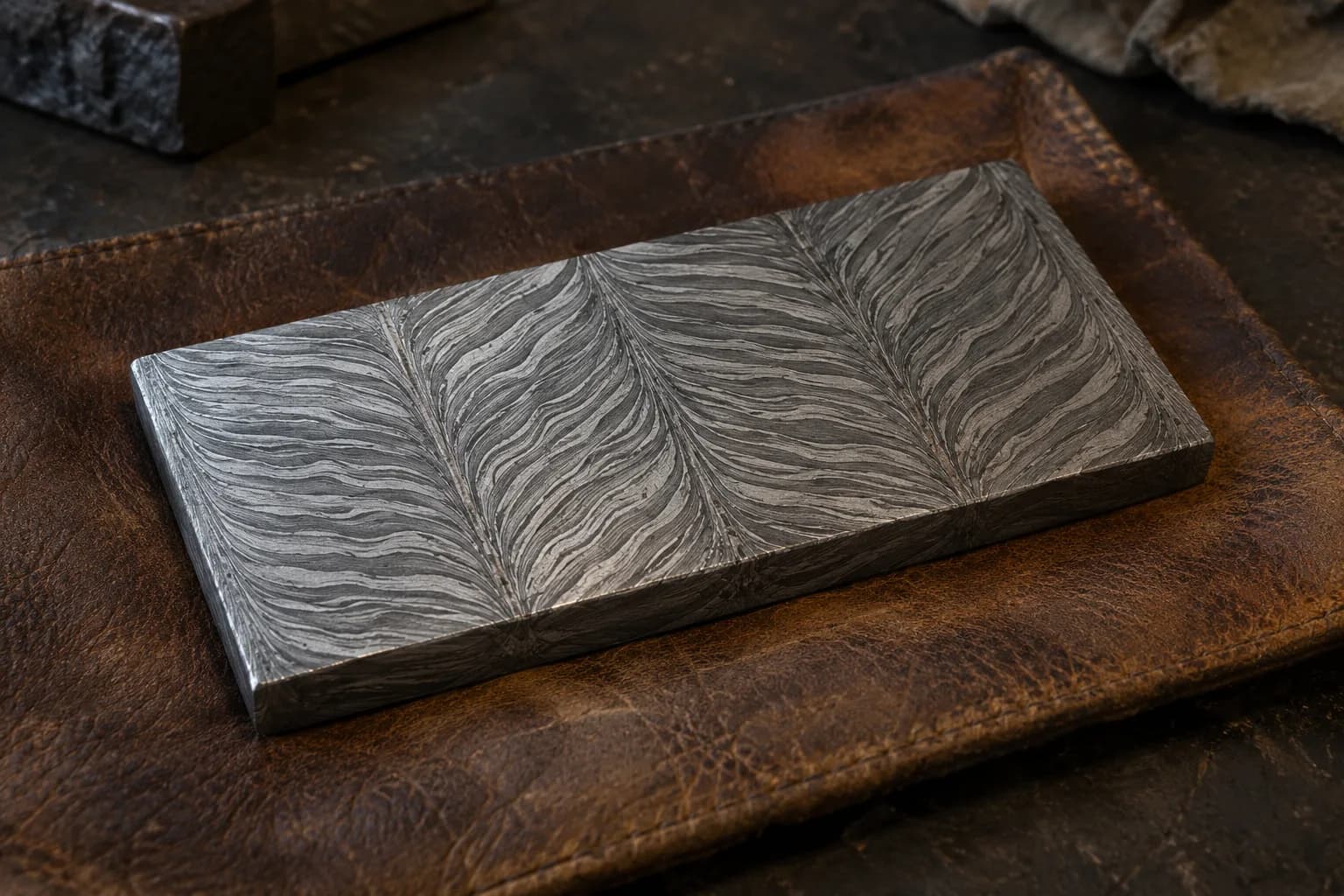 Etched flat steel coupon on a leather pad with four welded zones whose layers mirror at the seams in herringbone.