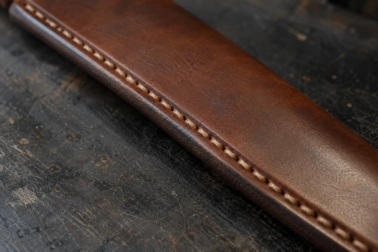 Close view of evenly spaced slanted tan saddle stitches seated in a groove along a smooth brown leather sheath seam.