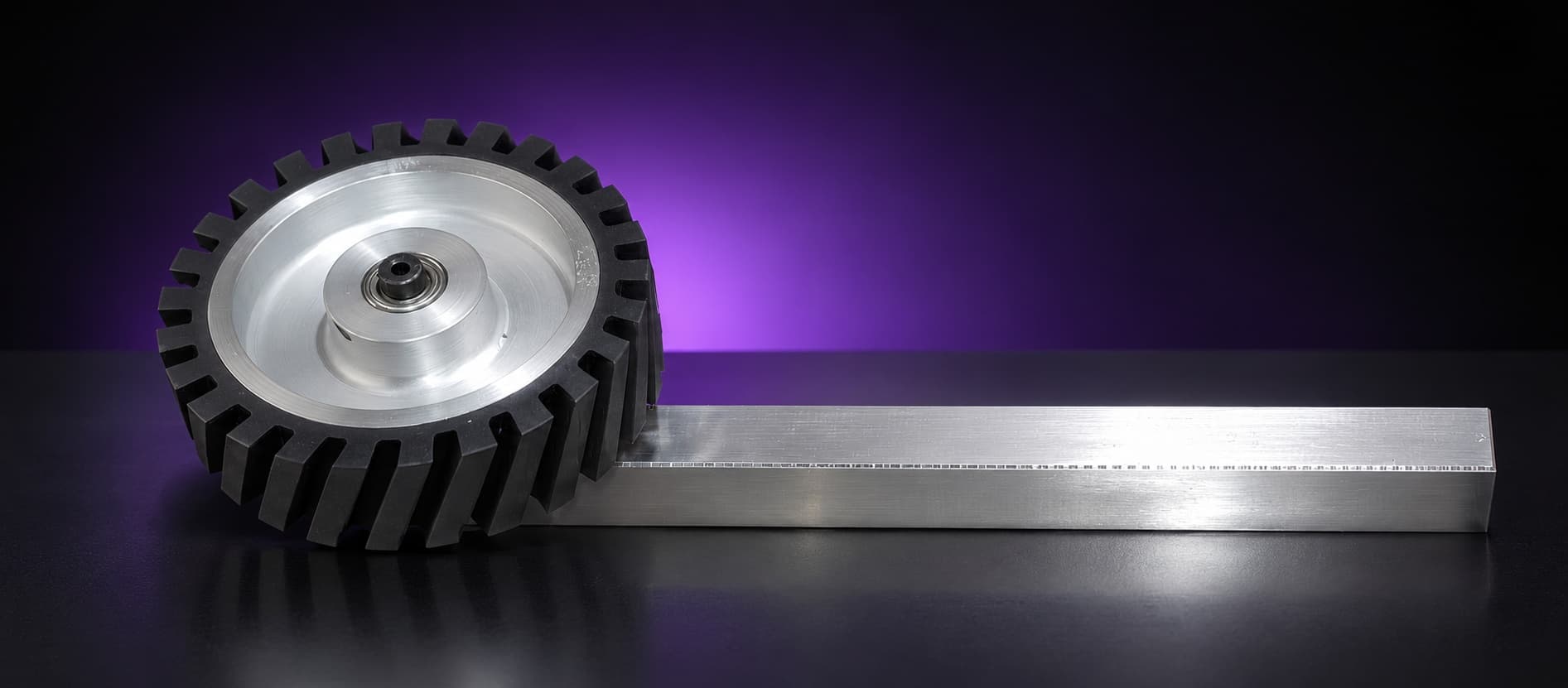 Serrated rubber contact wheel with aluminum hub and bearing on a square tooling arm, side view, on black with a purple glow