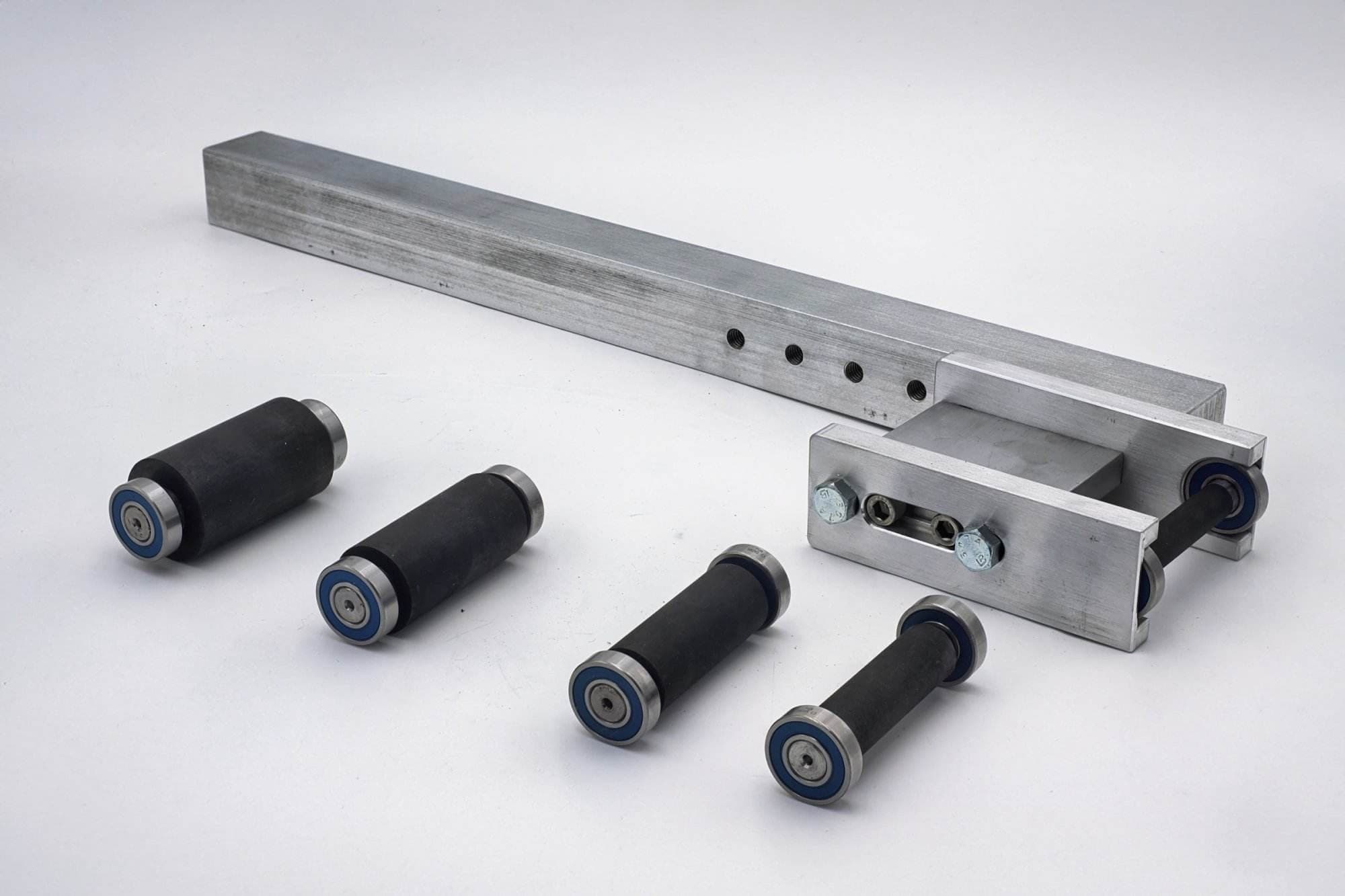 Aluminum bracket, drilled mounting plate, and five rubber-coated idler rollers arranged on a table