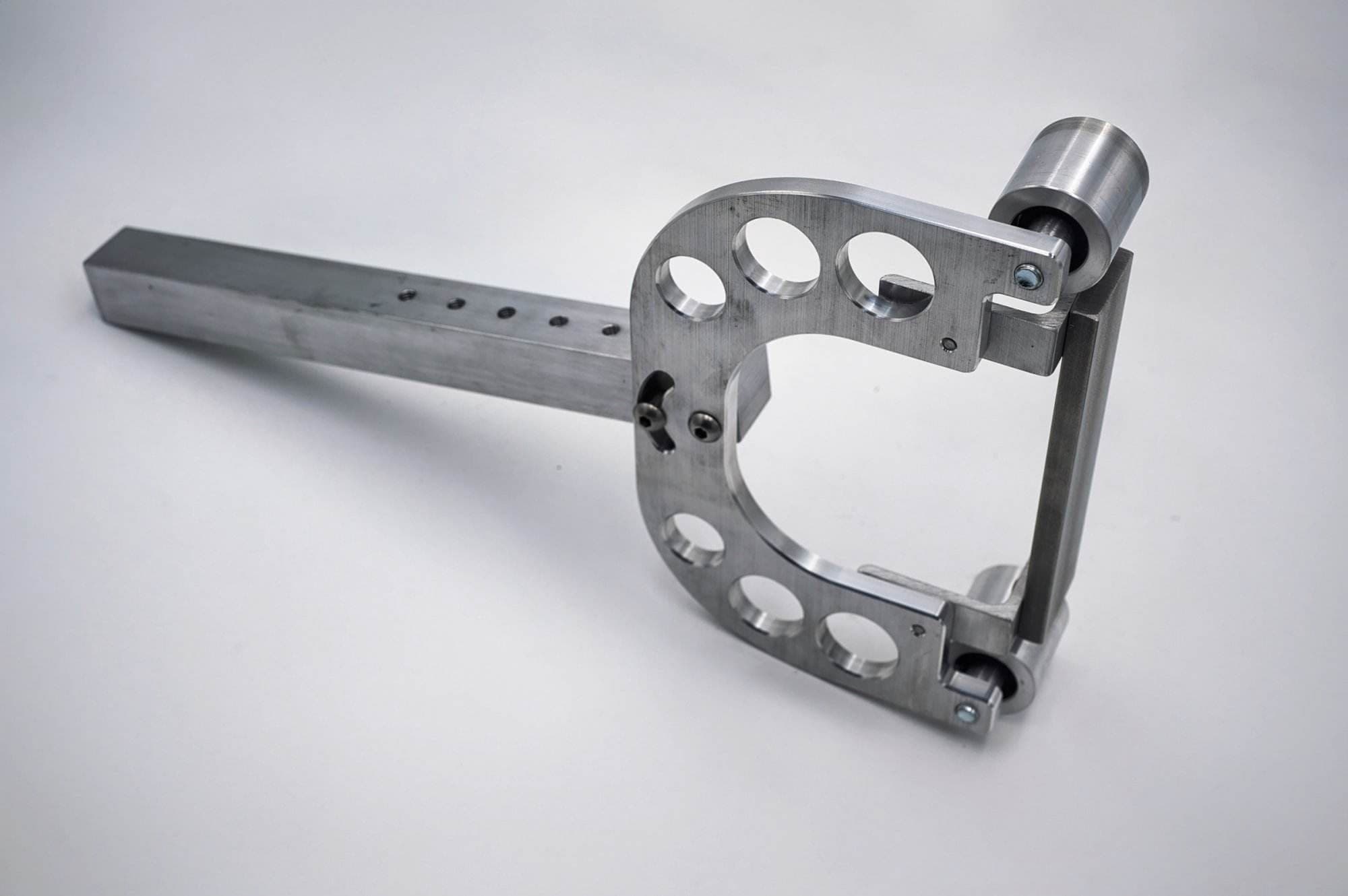CNC aluminum pivot bracket with paired rollers standing upright beside its square mounting bar