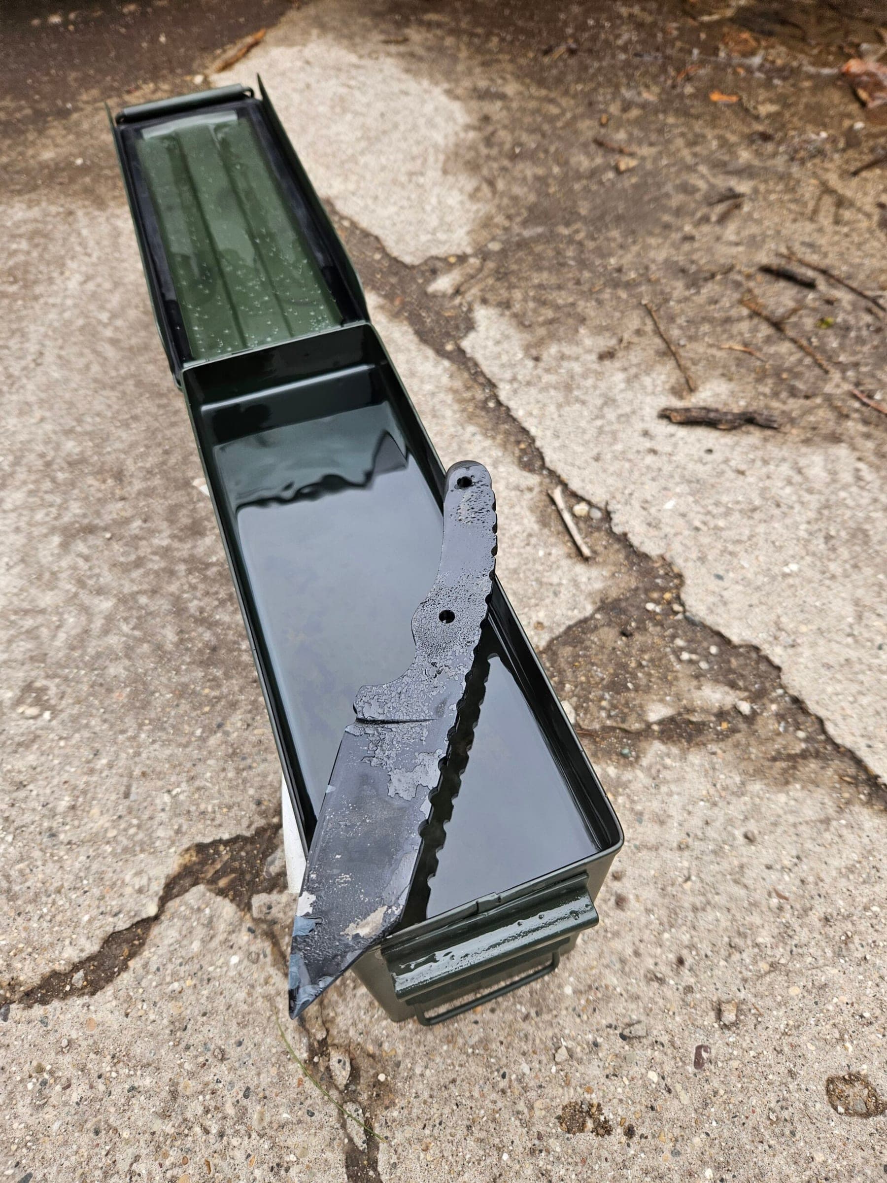 Open ammunition can used as an oil quench tank with a partially forged blade blank resting inside