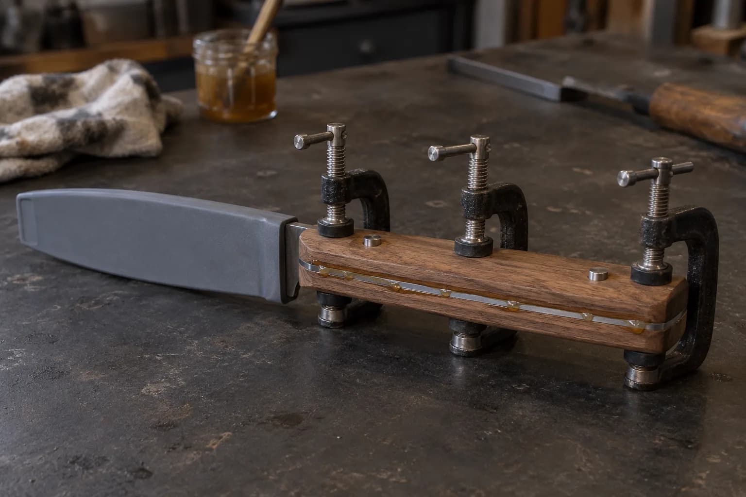 Three screw clamps spaced along a walnut handle on a dark bench, amber glue squeezing from the tang line, covered blade at left