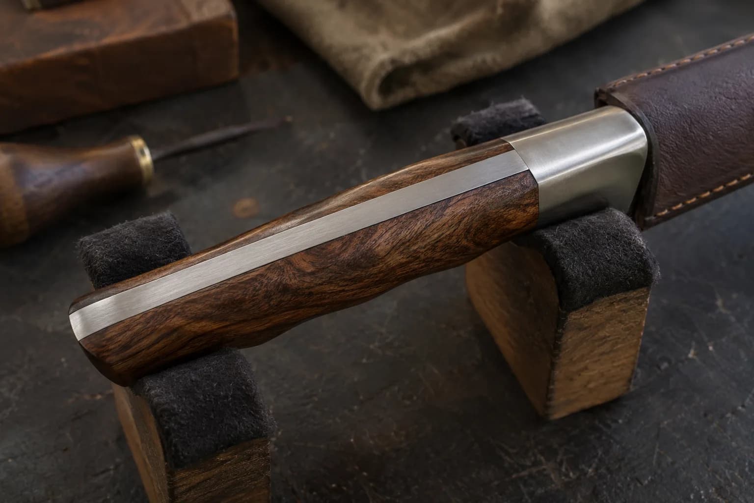 Spine view of a full-tang knife handle in padded cradles, steel bolster and wood scales shaped flush as one contour