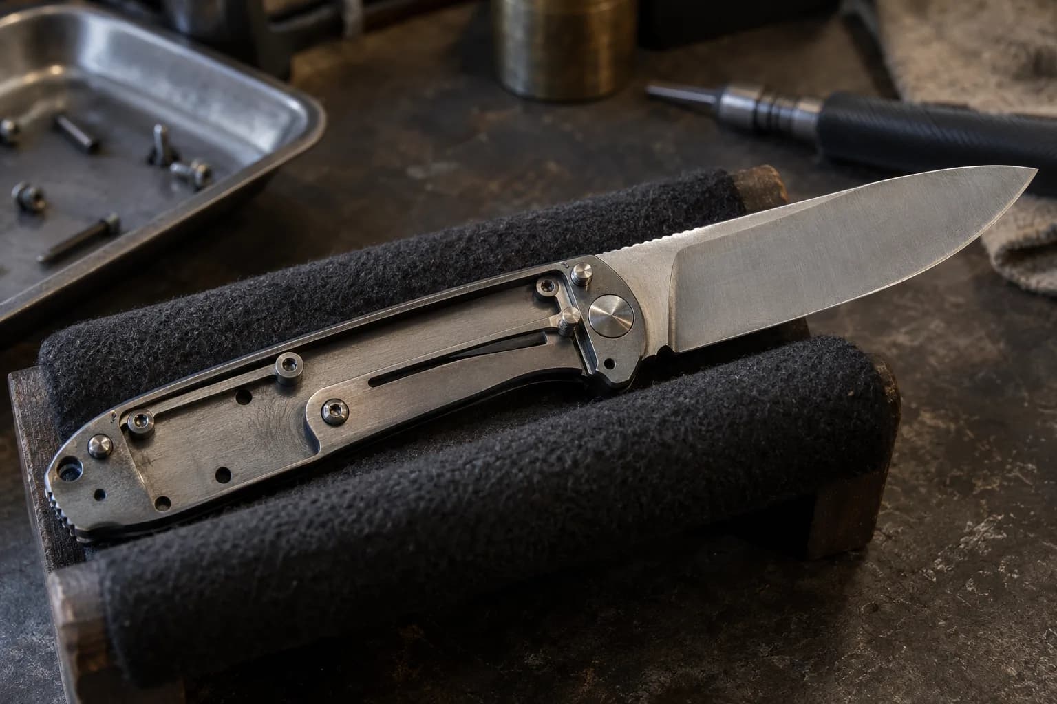 Open folding knife in a felt cradle with one handle scale removed, showing the slotted liner and pivot beside a screw tray