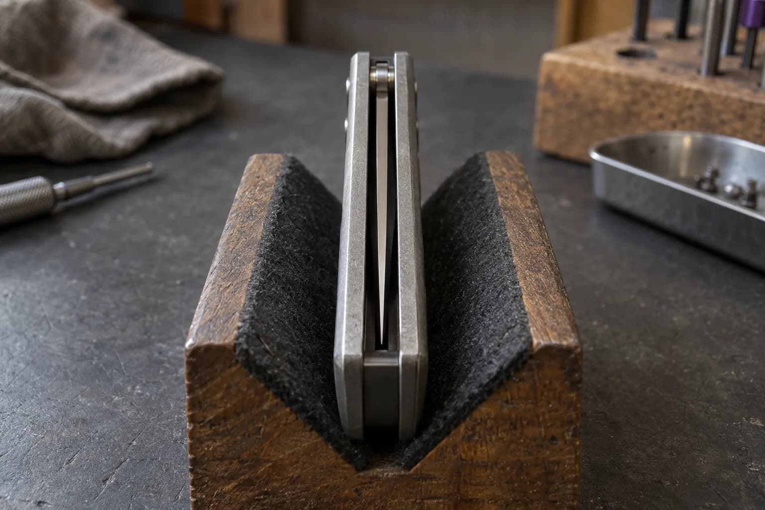 End-on view down the channel of a closed folding knife in a felt-lined V-block, blade centered between liners with tip buried.