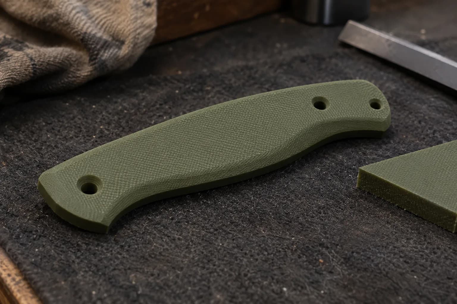 Olive green G10 handle scale with a contoured top and three pin holes, beside a cut offcut of the same solid color.