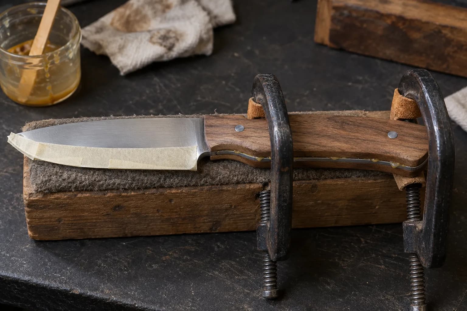 Walnut-handled knife with taped edge, scales clamped to the tang by two iron C-clamps, epoxy squeezing out along the seam