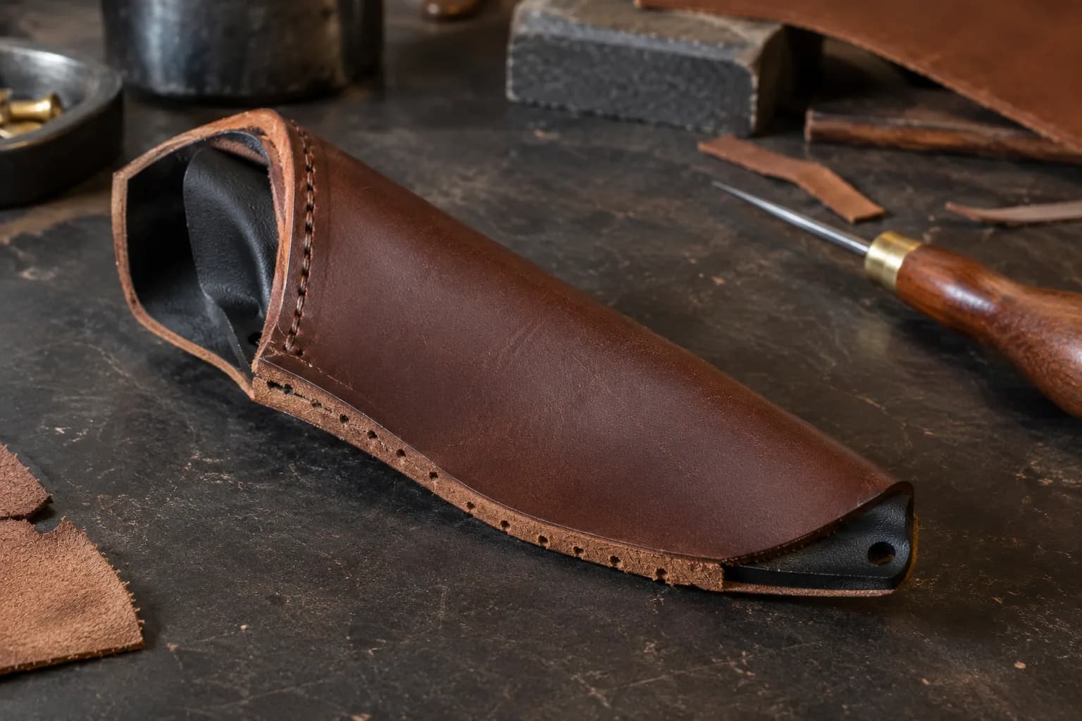 Black molded sheath liner seated inside an open leather sheath body, with punched stitch holes along one edge and an awl nearby.