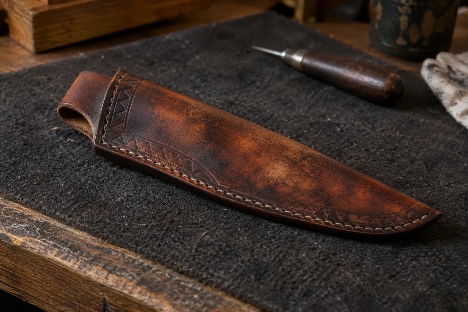 Stitched leather sheath on dark felt with pale mottled patches mid-panel and darker dye near the edges and seam.