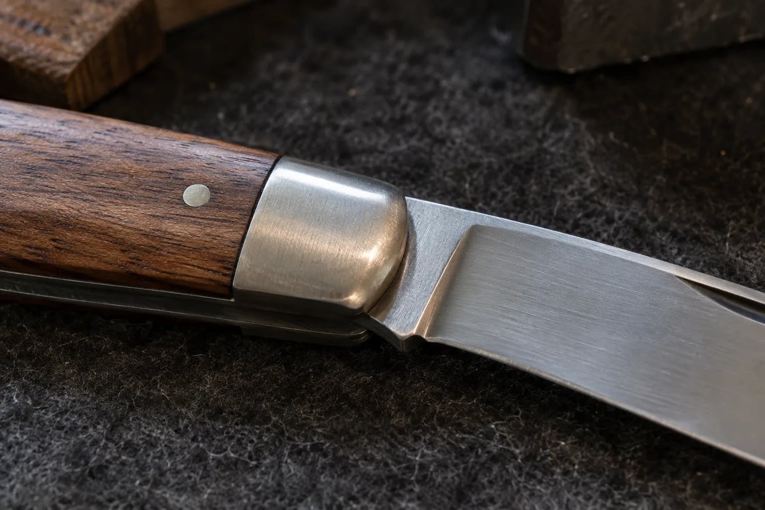 Open traditional pocketknife on dark felt, close on its satin bolster, walnut handle scale and blade heel.