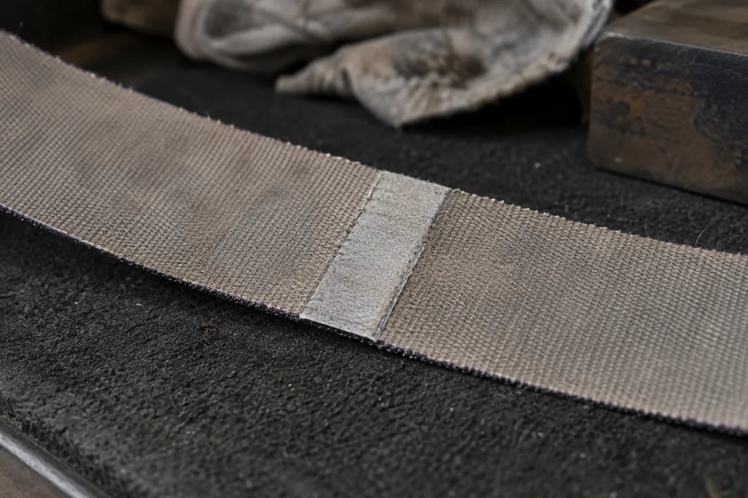 Taped splice joint across the cloth backing of a fine abrasive belt lying on a dark felt bench pad