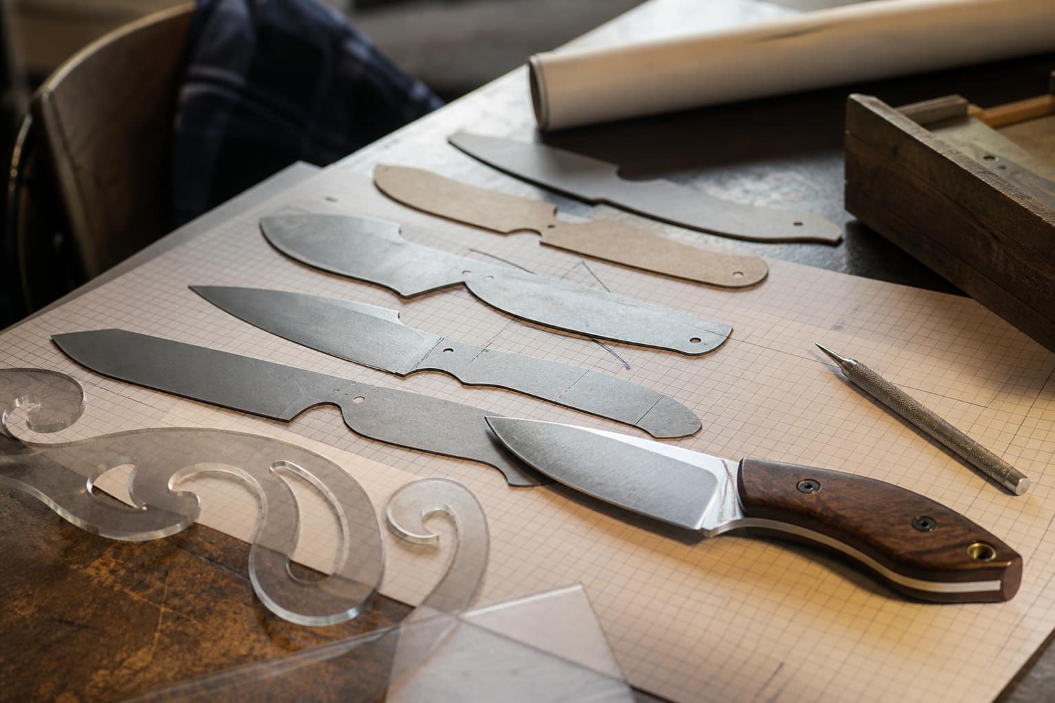 Knife profile templates cut from metal and plastic laid over graph paper beside a finished knife