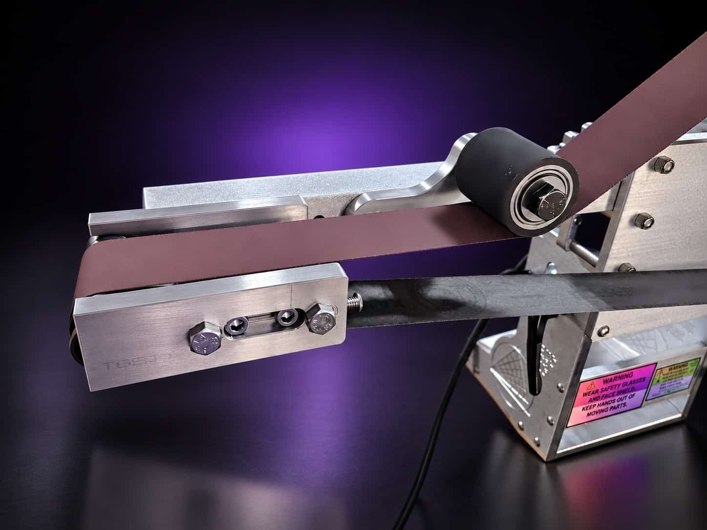 Grinder with the small wheel attachment on a square arm, rubber idler roller and belt fitted, on black with a purple glow
