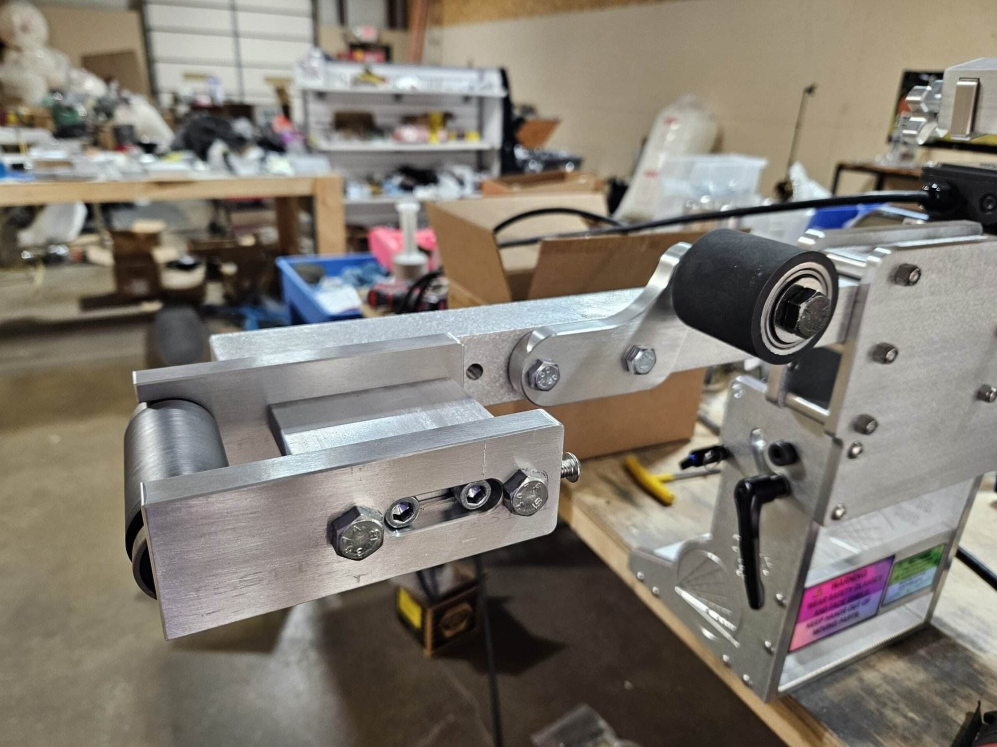 Small wheel attachment mounted on a 2x72 belt grinder inside a cluttered home workshop