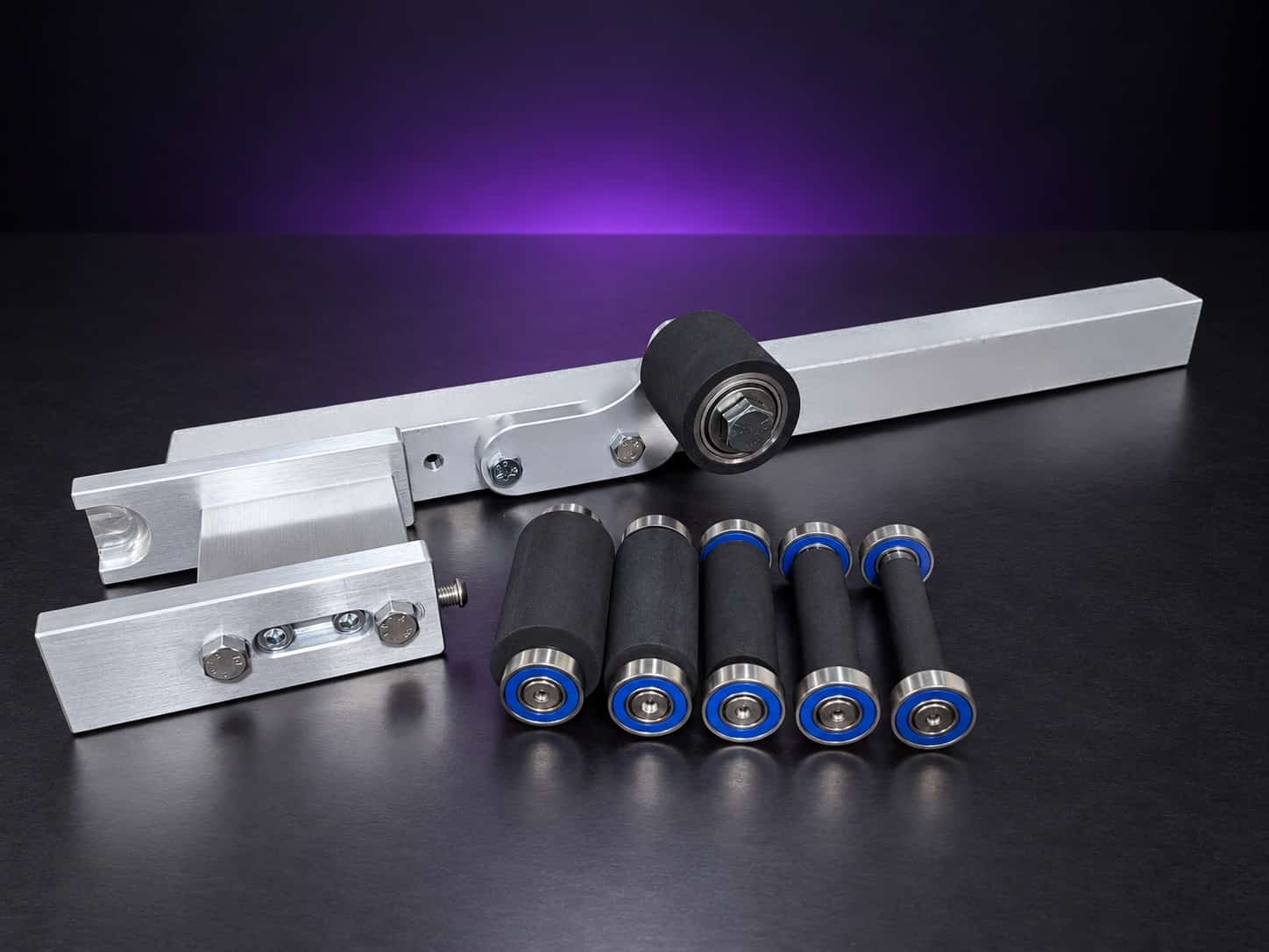 Small wheel attachment kit laid out: arm, holder, side plate, idler roller and five wheels, on black with a purple glow
