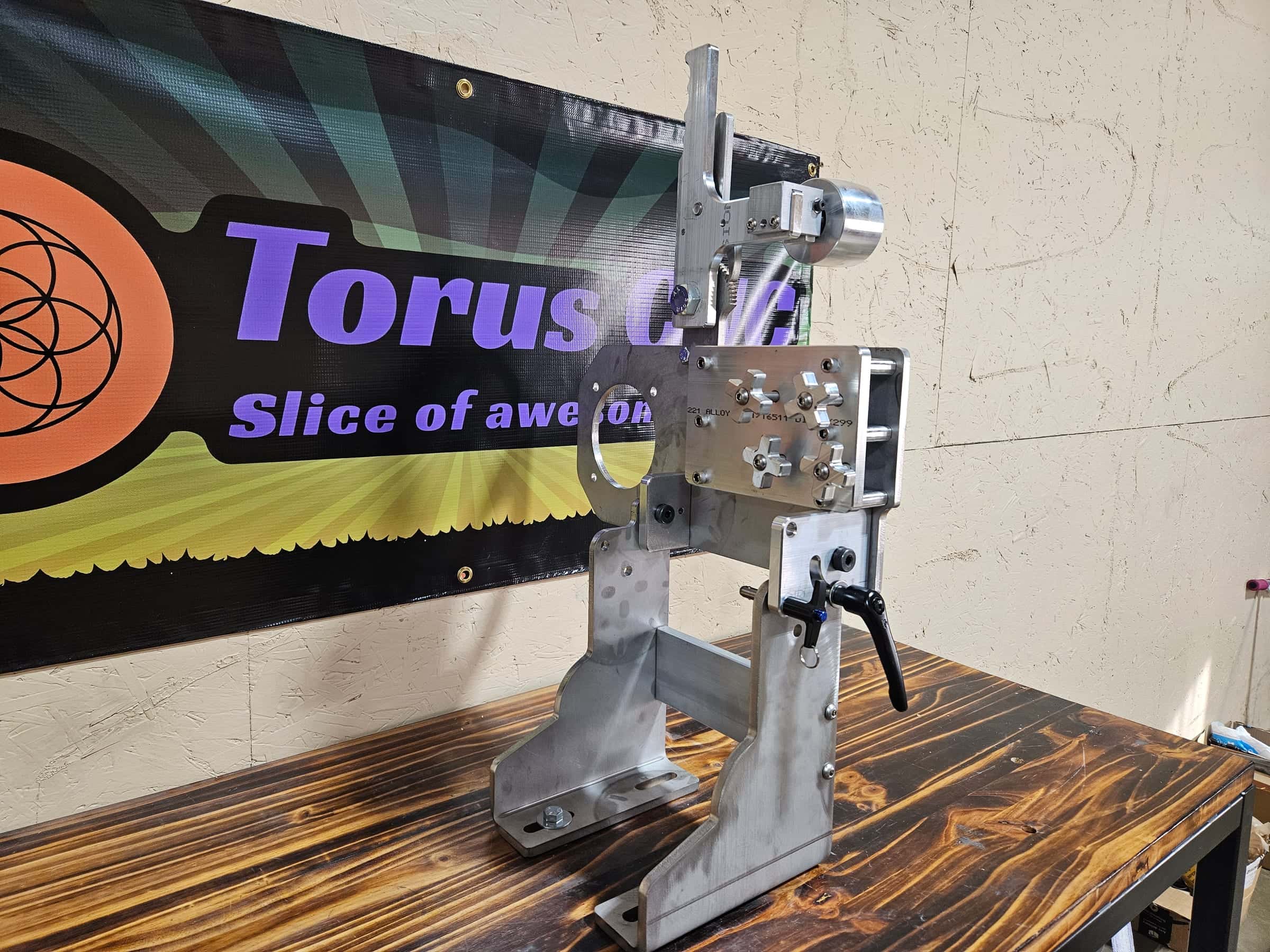 Front view of a Torus CNC aluminum belt grinder arm showing knurled adjustment knobs and a 221 alloy stamp