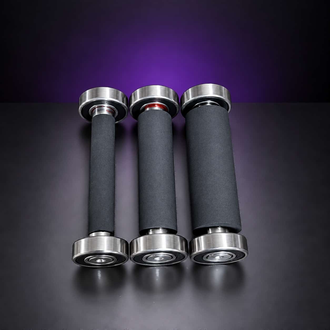 Three black rubber small wheels on bearings, from narrow to wide, standing in a row, on black with a purple glow