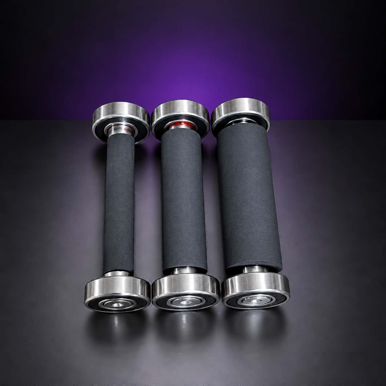 Three black rubber small wheels on bearings, from narrow to wide, standing in a row, on black with a purple glow