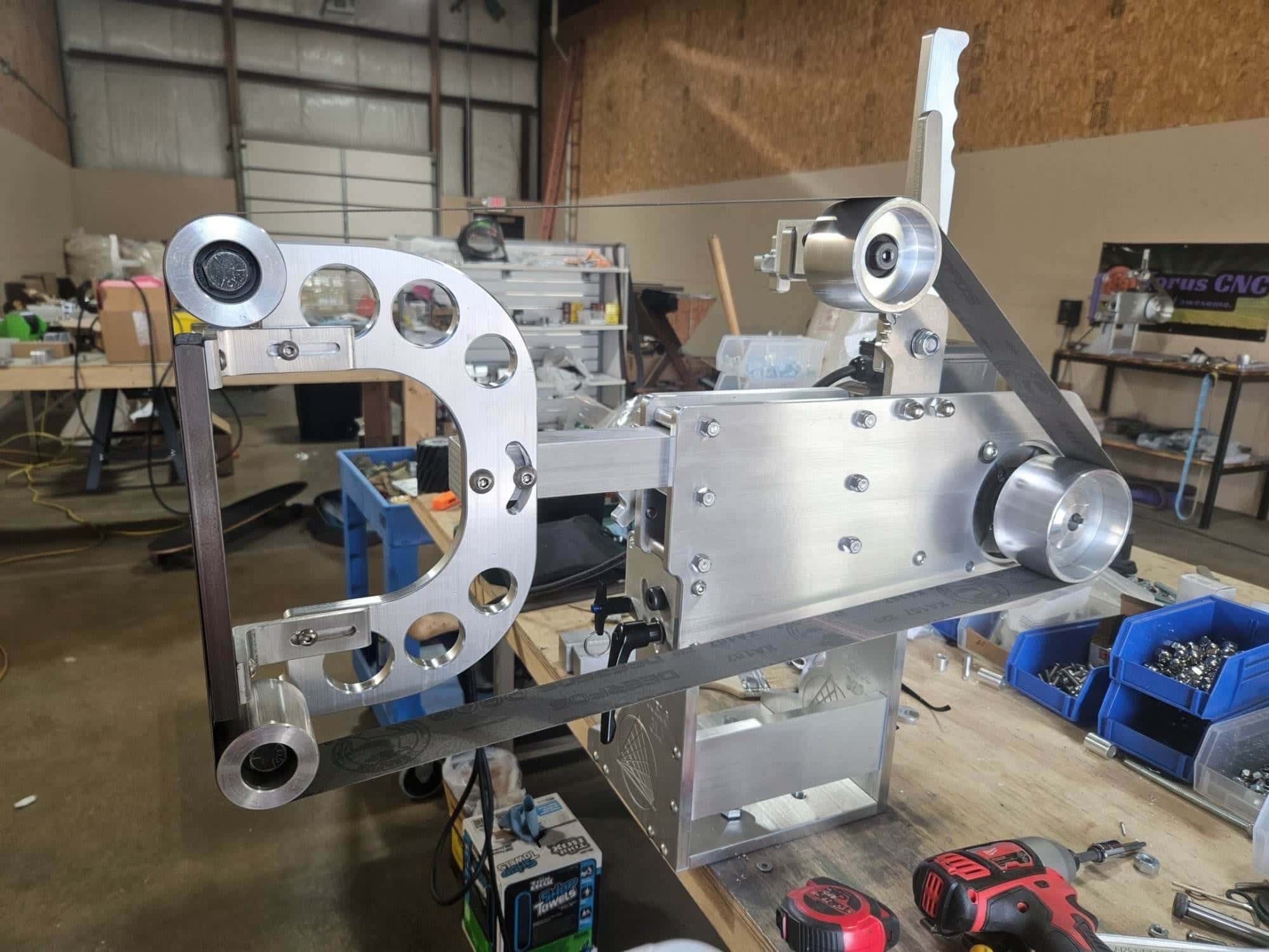 Aluminum tooling arm and belt tensioner assembly mounted on a grinder in a metal shop