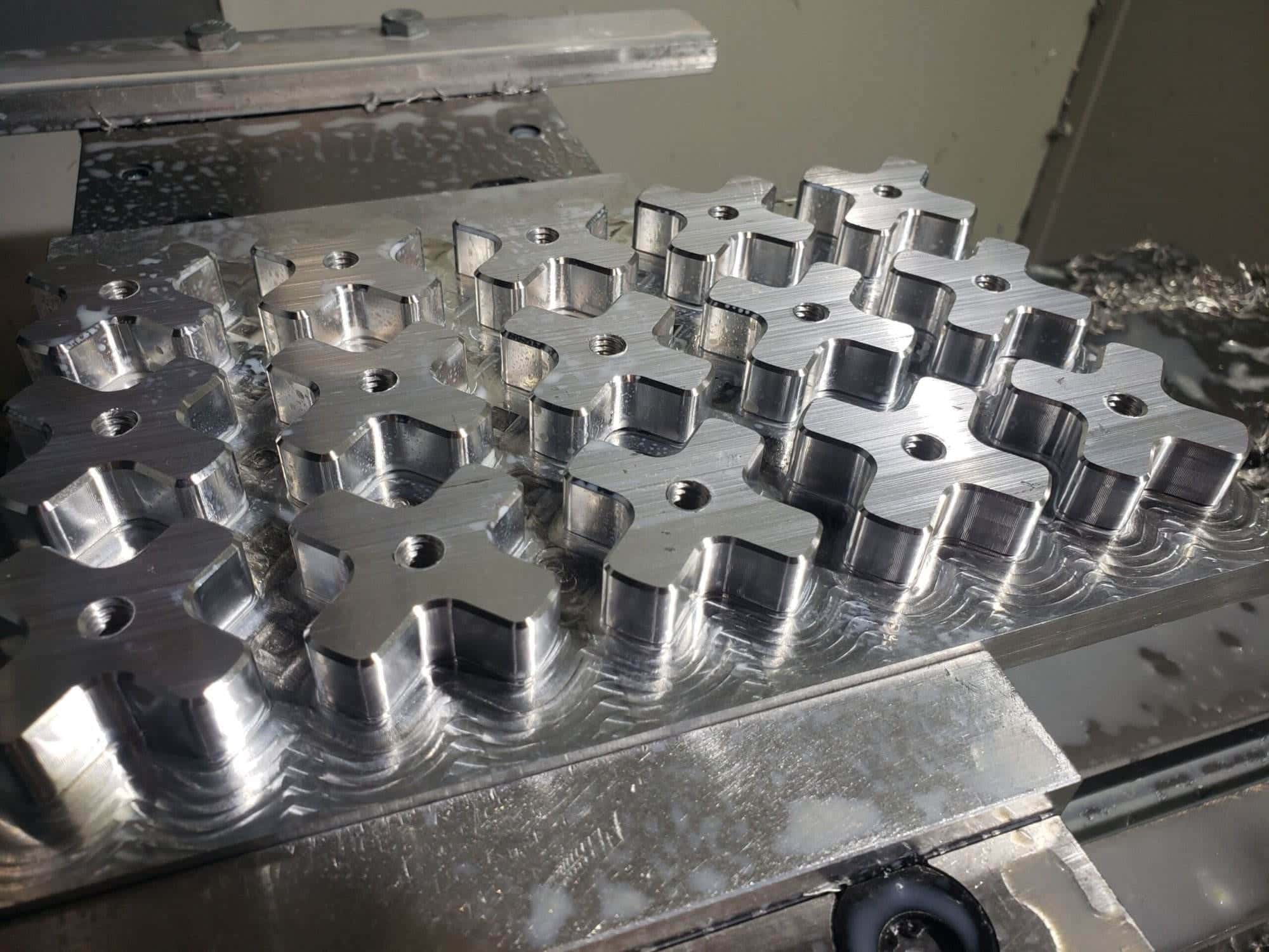 Freshly milled aluminum stock with rows of cross-shaped tension knob blanks on the mill table