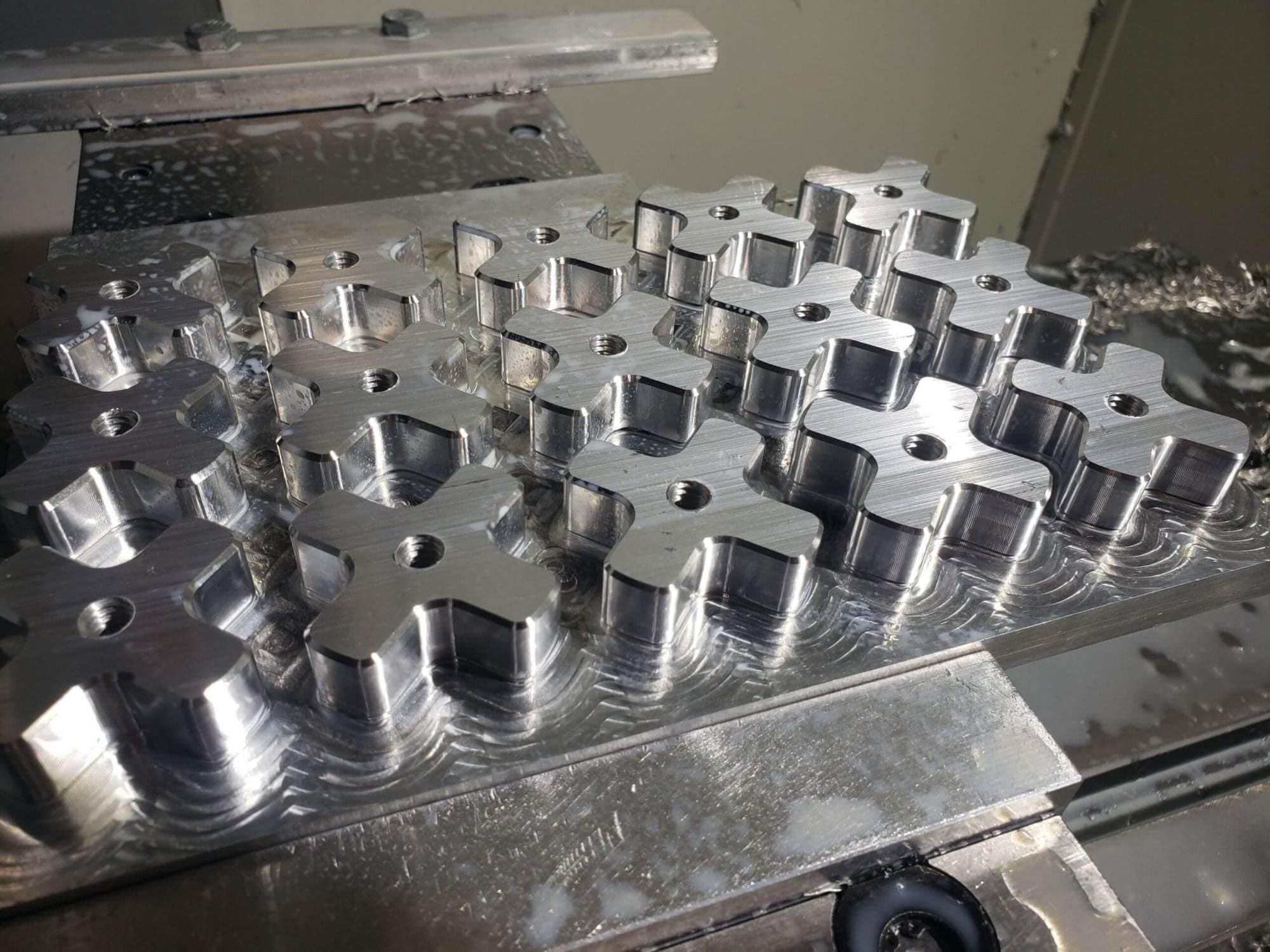 Freshly milled aluminum stock with rows of cross-shaped tension knob blanks on the mill table