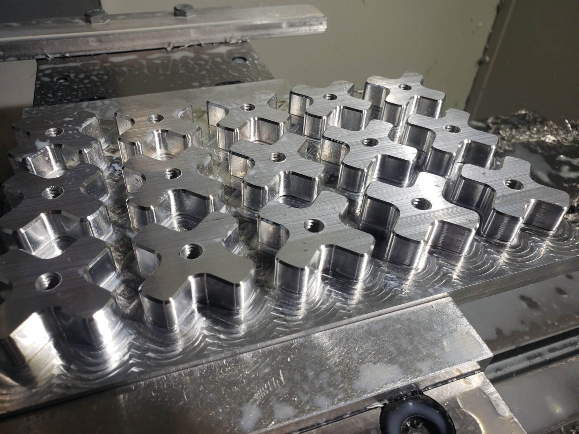 Freshly milled aluminum stock with rows of cross-shaped tension knob blanks on the mill table