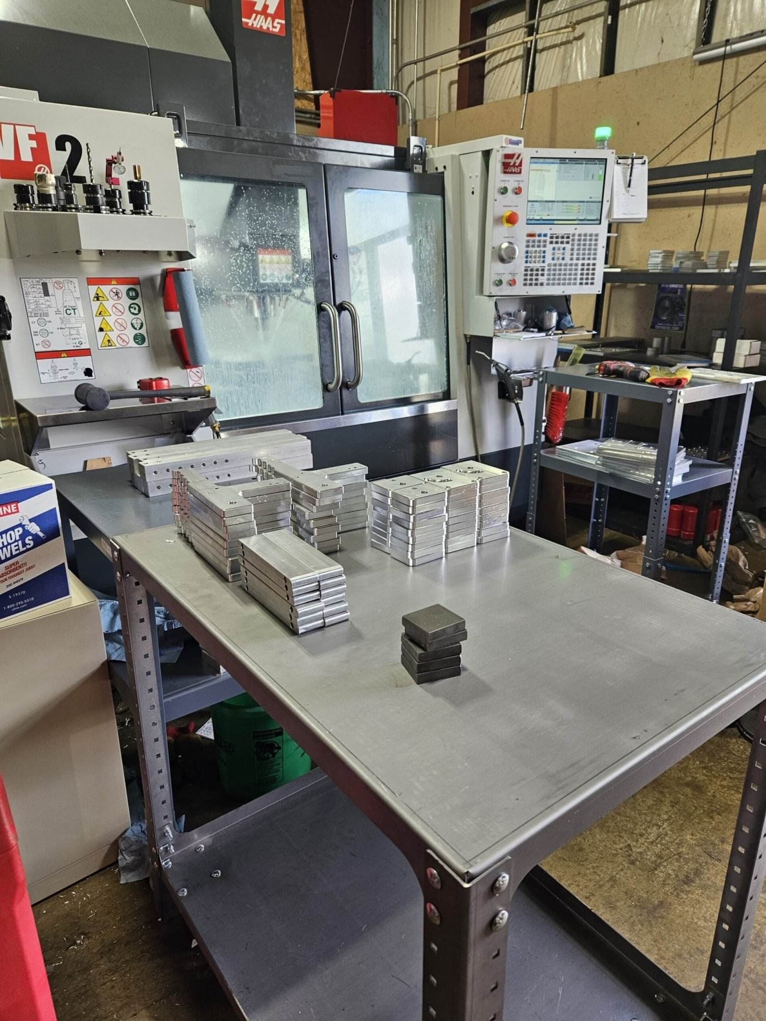 Haas VF-2 CNC mill with stacks of machined aluminum tooling-arm blanks on the shop workbench