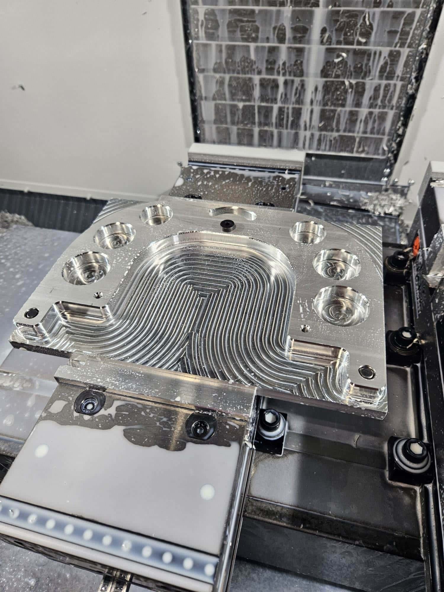 Freshly CNC-machined aluminum mounting plate with coolant droplets sitting on the mill table