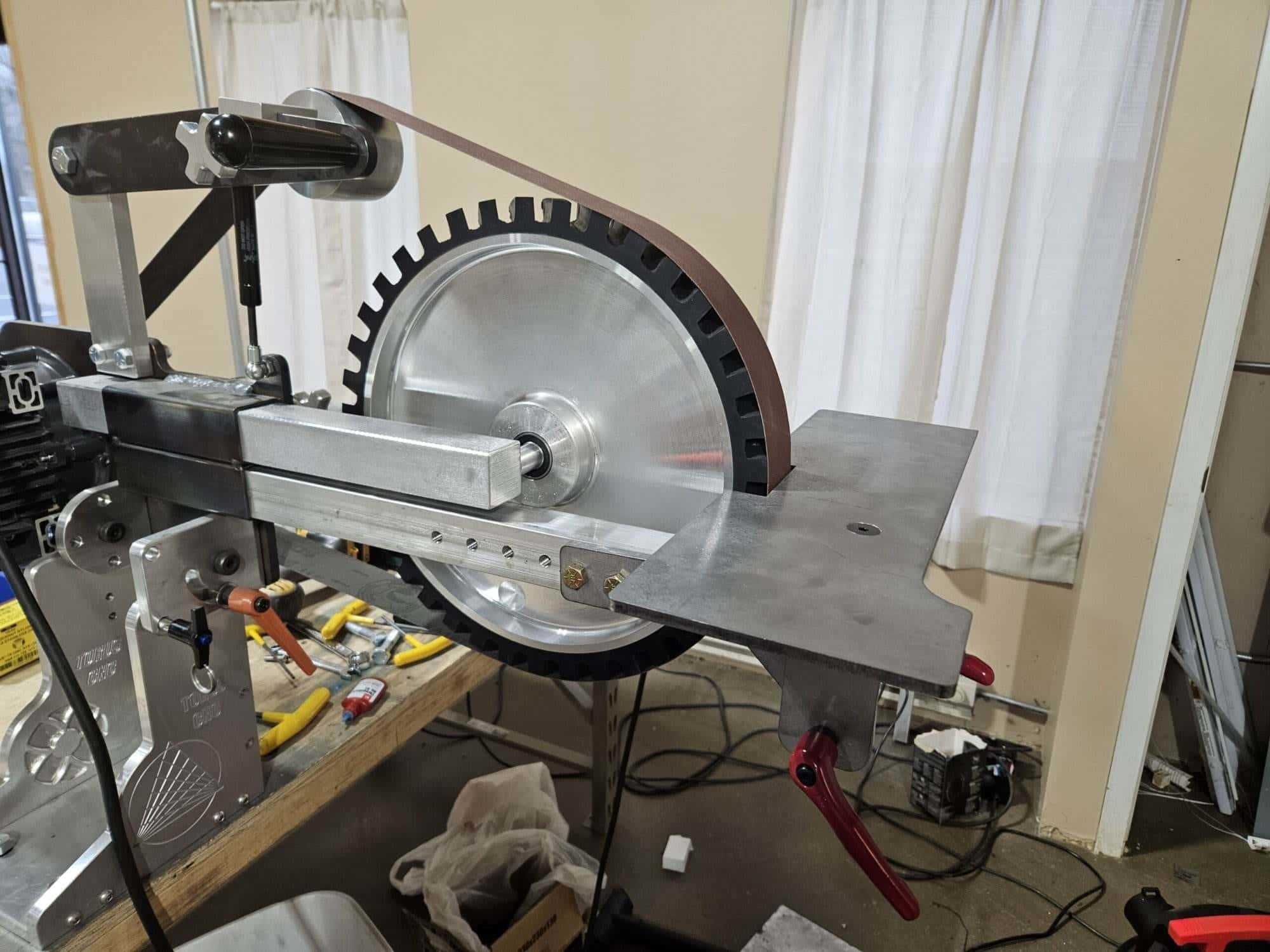 Large aluminum contact wheel and abrasive belt mounted on a Torus CNC grinder frame near a window