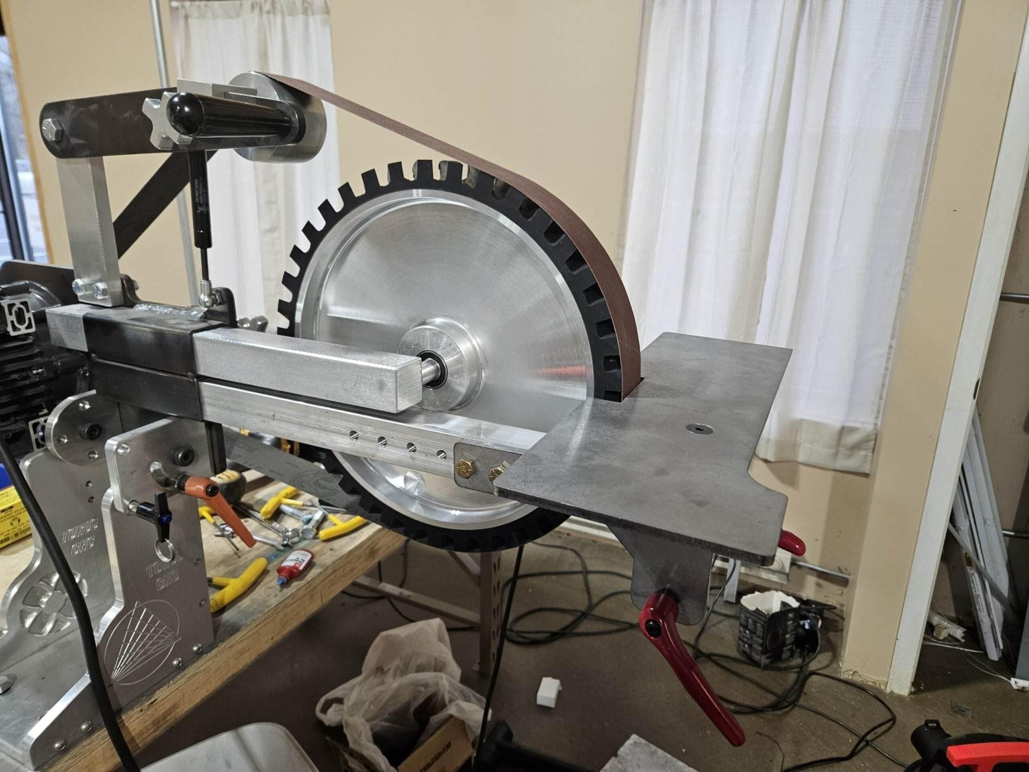 Large aluminum contact wheel and abrasive belt mounted on a Torus CNC grinder frame near a window