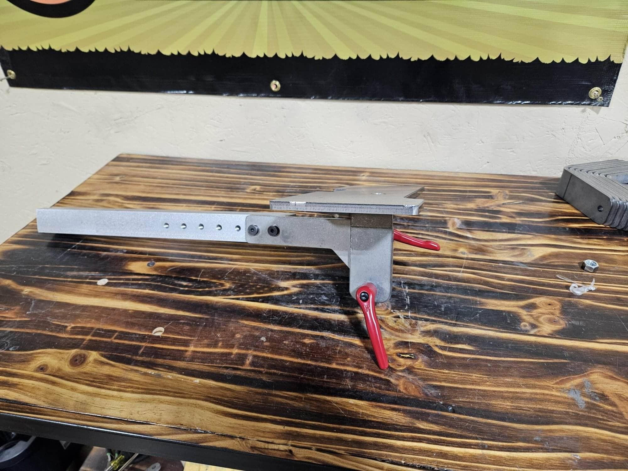 The aluminum adjustable work table attachment with its red locking levers on a wood bench