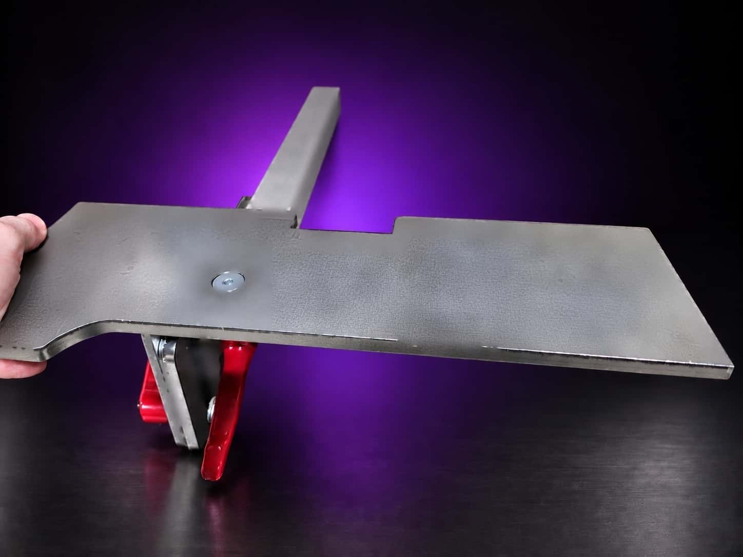 Work table plate from the side, showing its bracket, red cam levers and square arm bar, on black with a purple glow