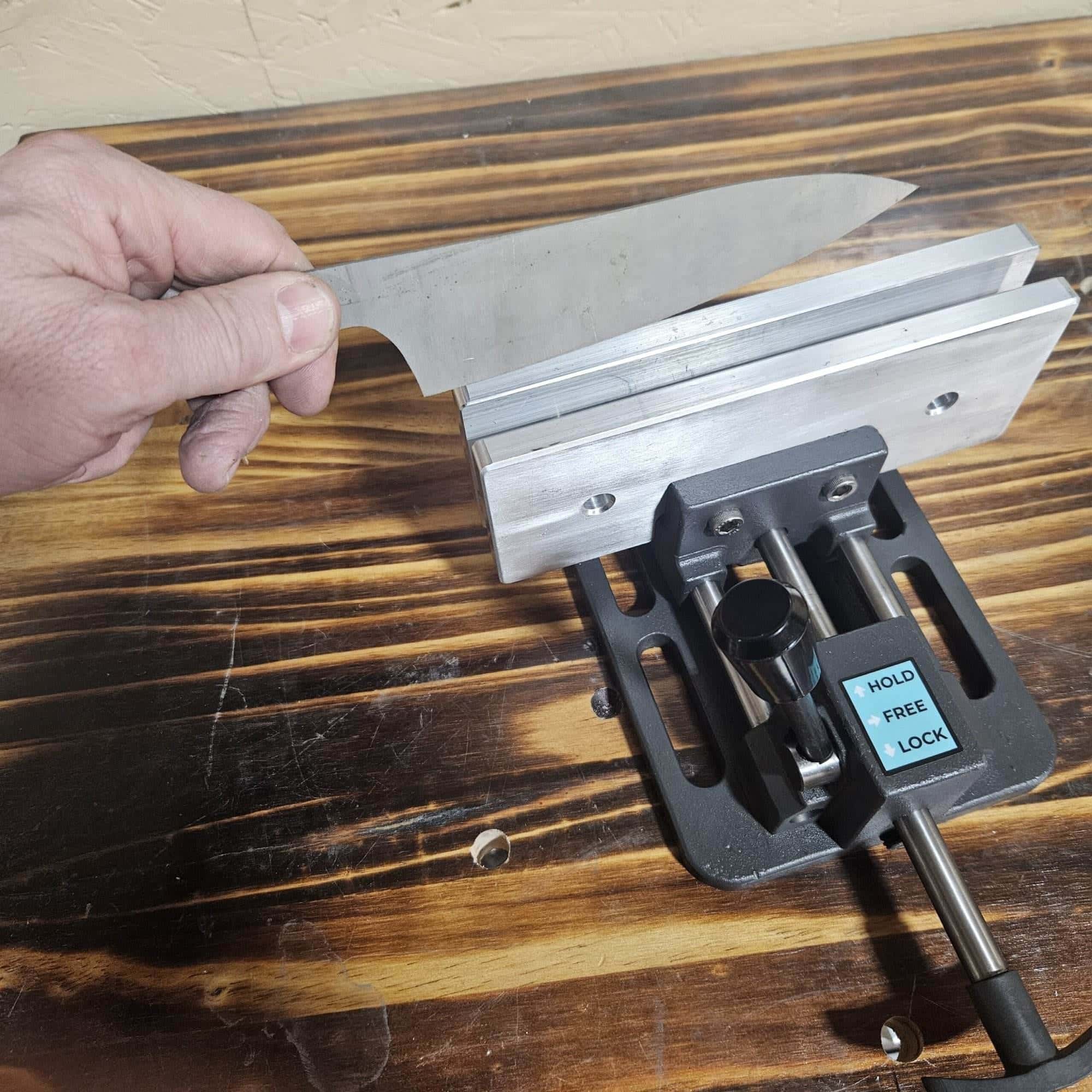 Hand holding a knife blade over the open jaws of a Torus CNC quick quench vise on a bench