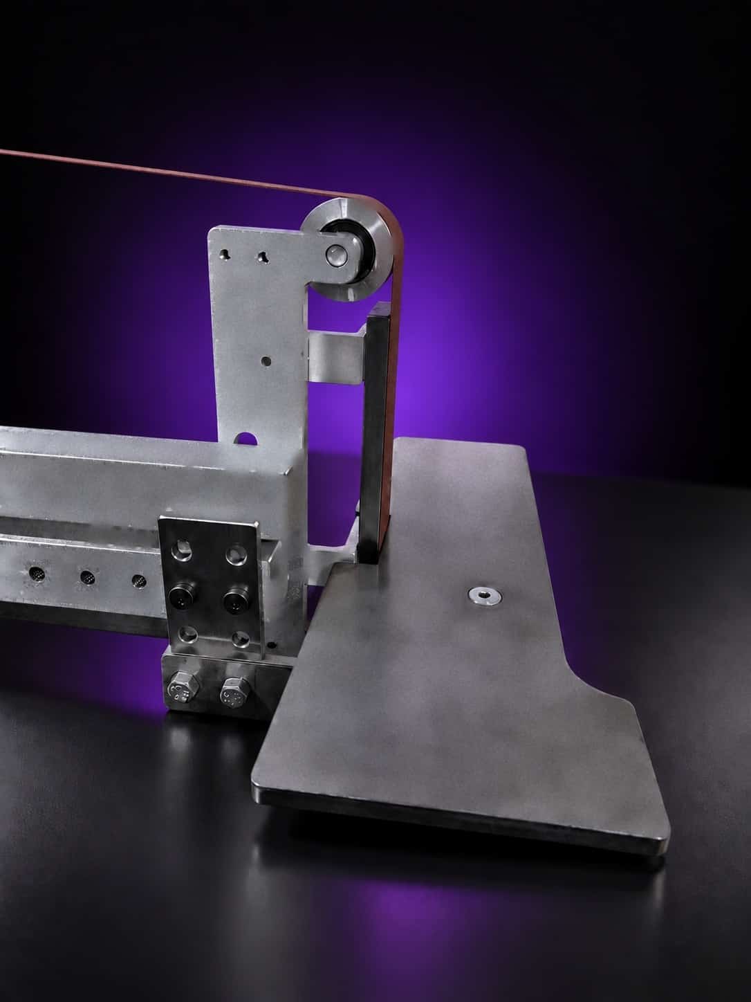 Steel work table mounted on the tool arm beside the platen and top idler wheel, close-up, on black with a purple glow