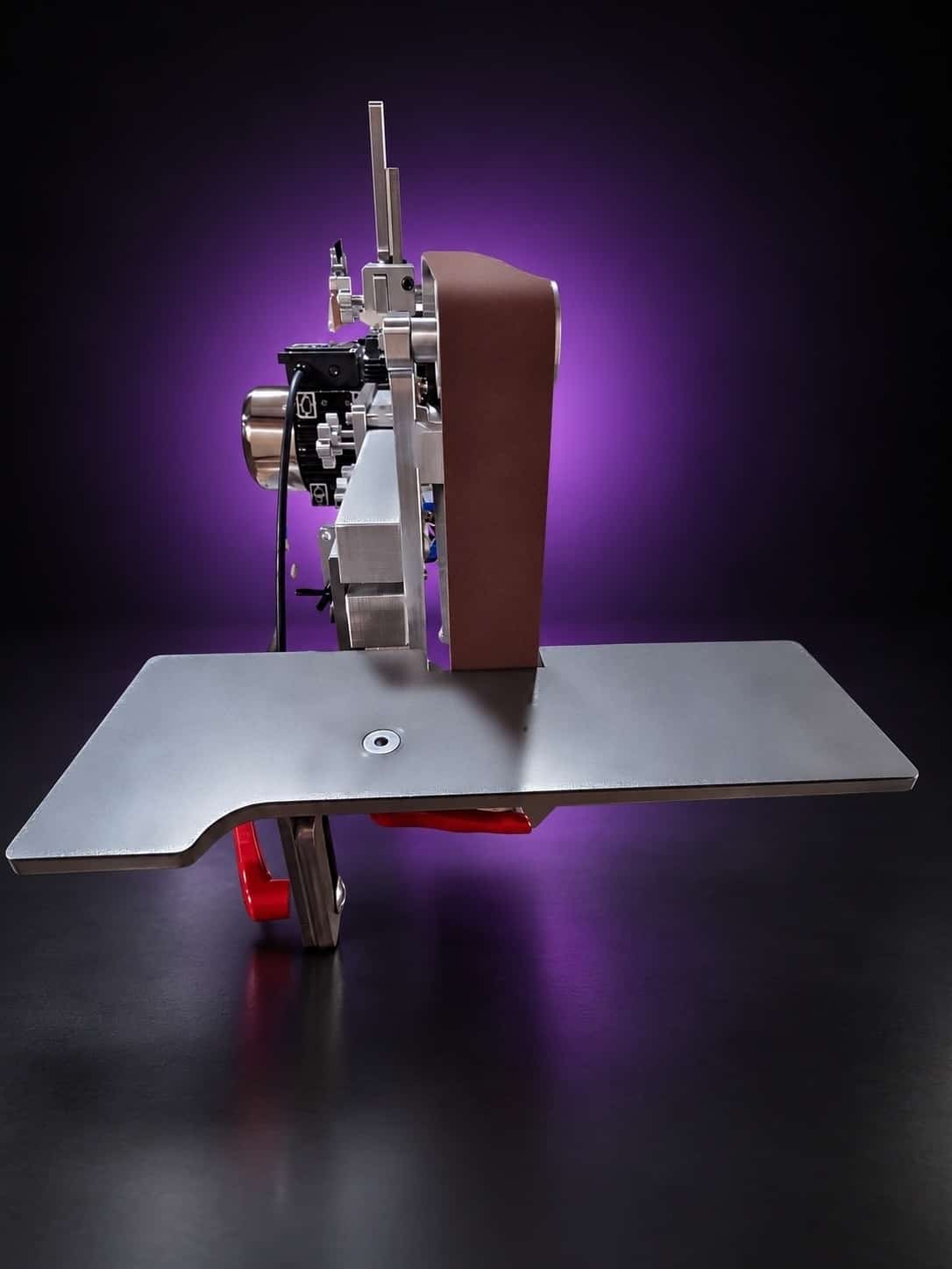 Work table in front of the belt, side-on view, with red cam levers under the plate, on black with a purple glow