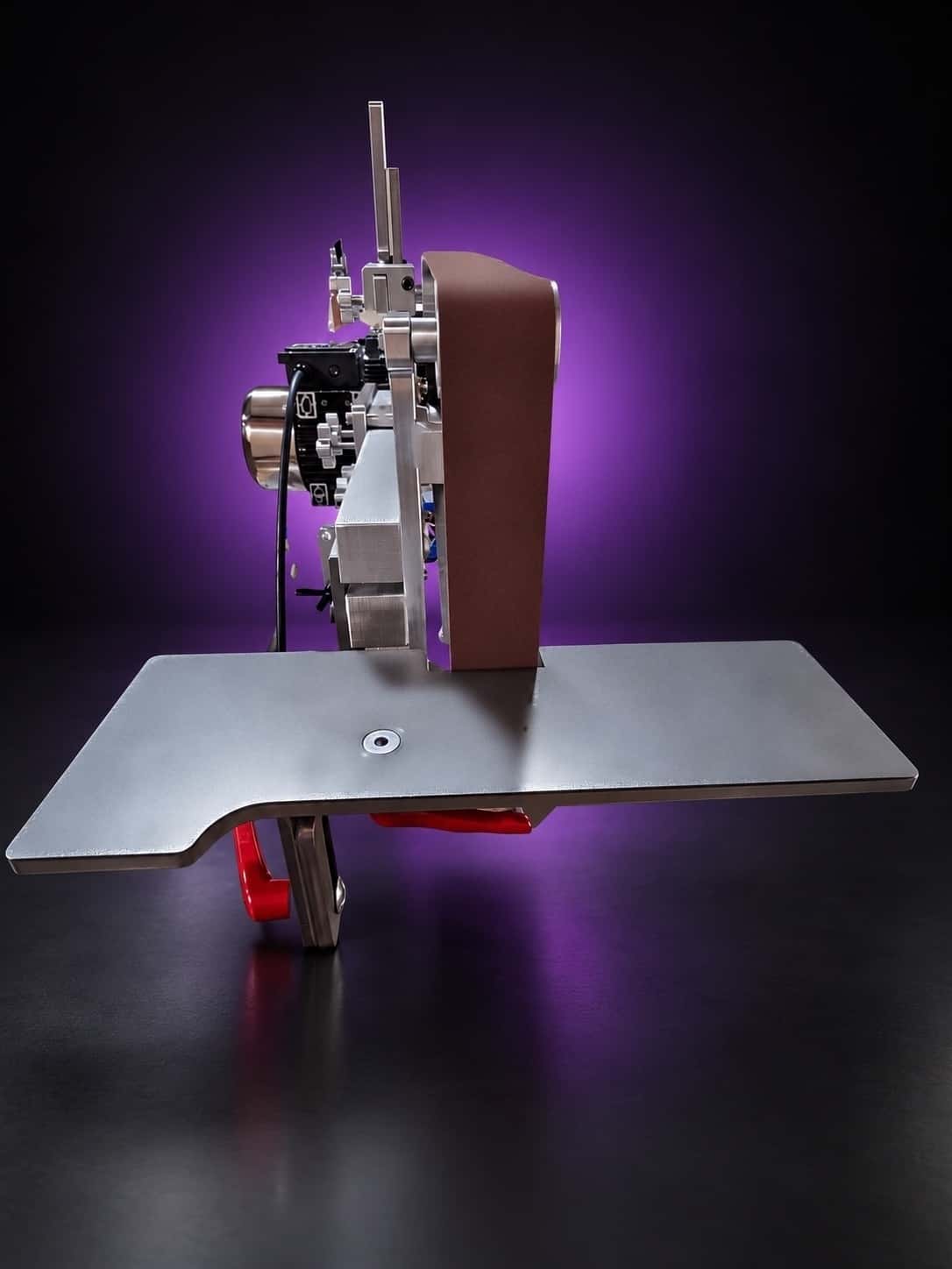 Work table in front of the belt, side-on view, with red cam levers under the plate, on black with a purple glow